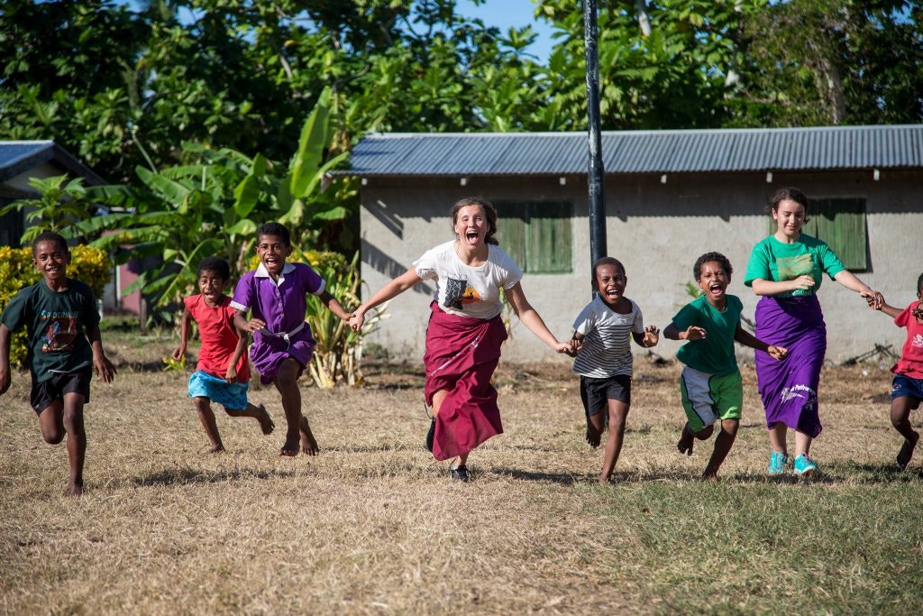 Children and foreign students running and playing together in a Fijian village