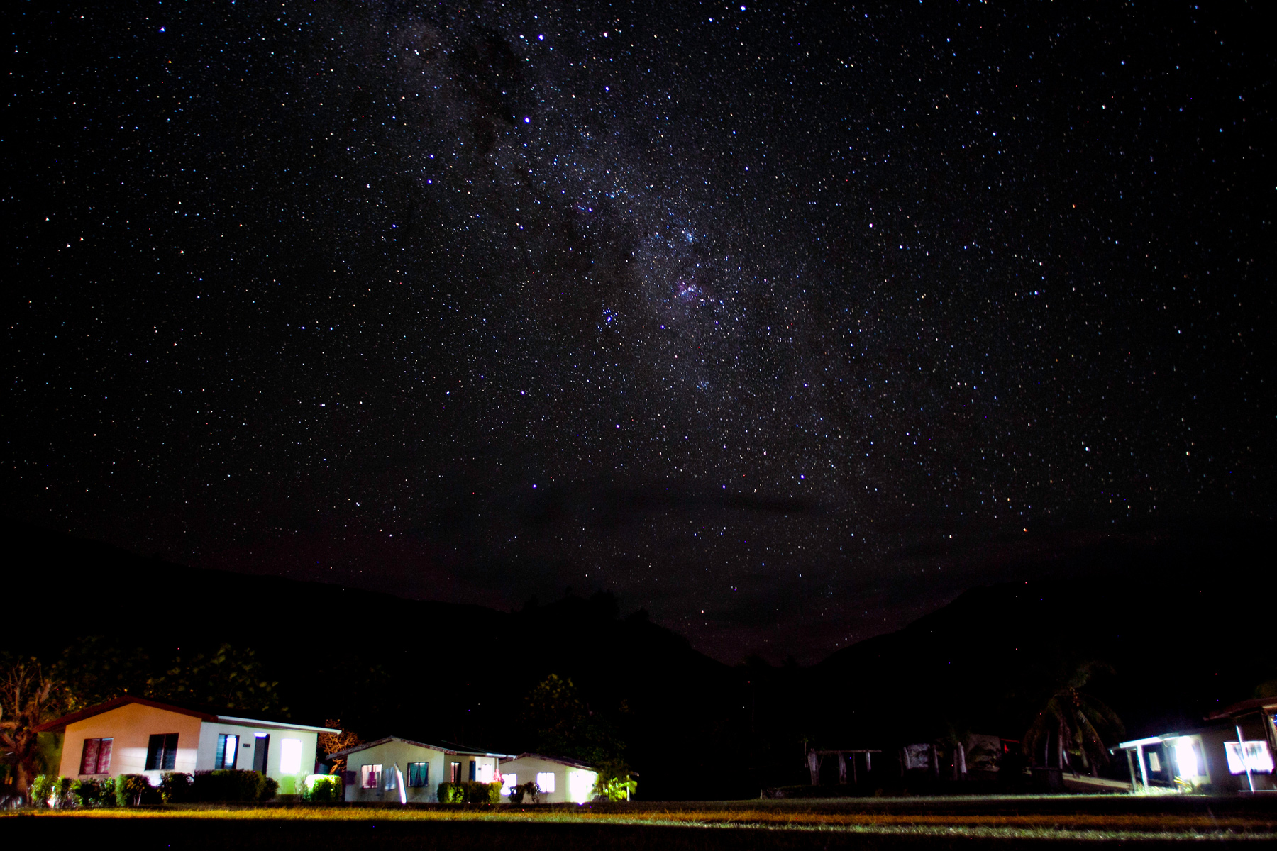The Milky Way glows over dark hillside cottages at night