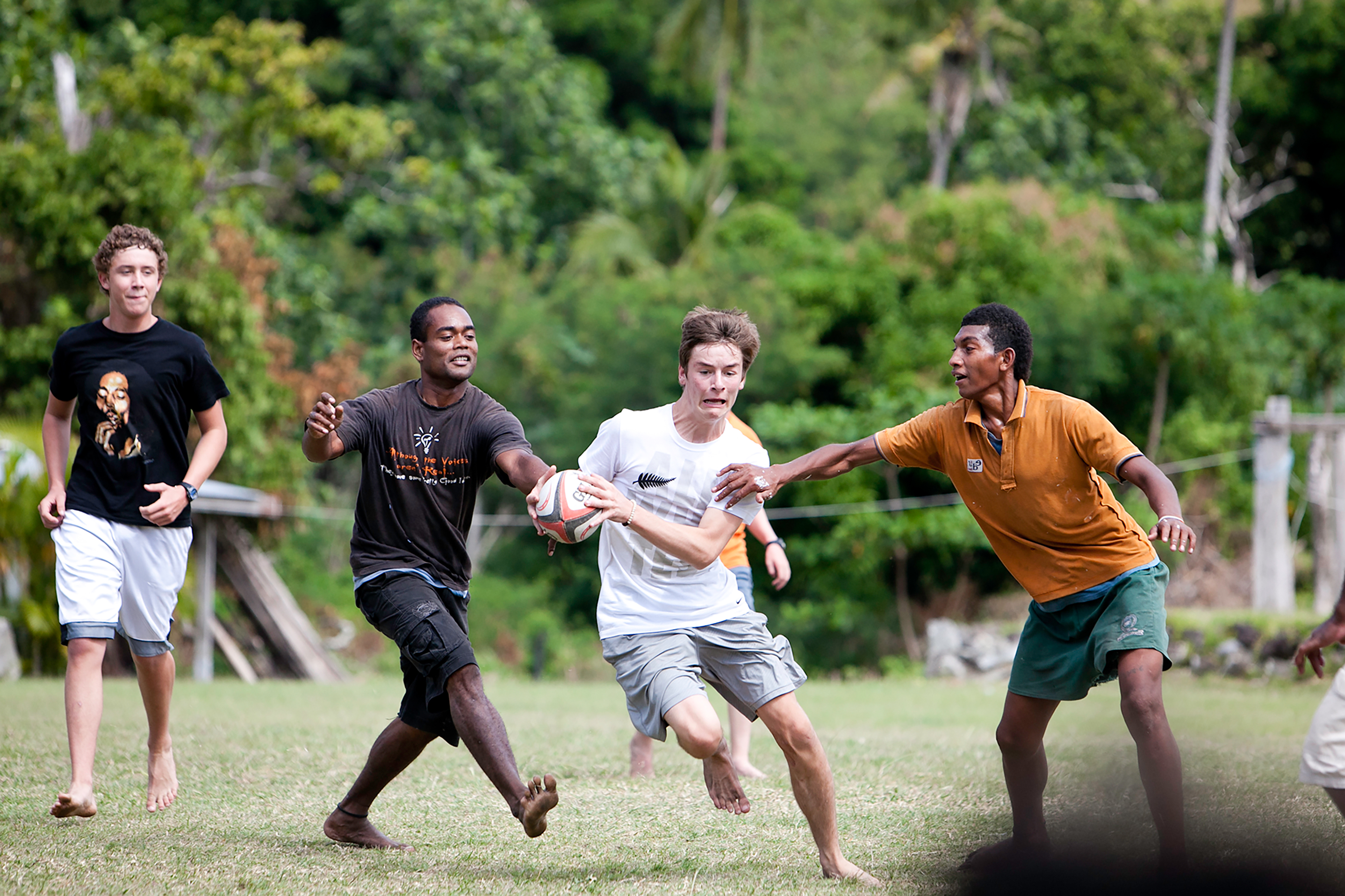 Students play rugby with local players on a grassy field in Fiji