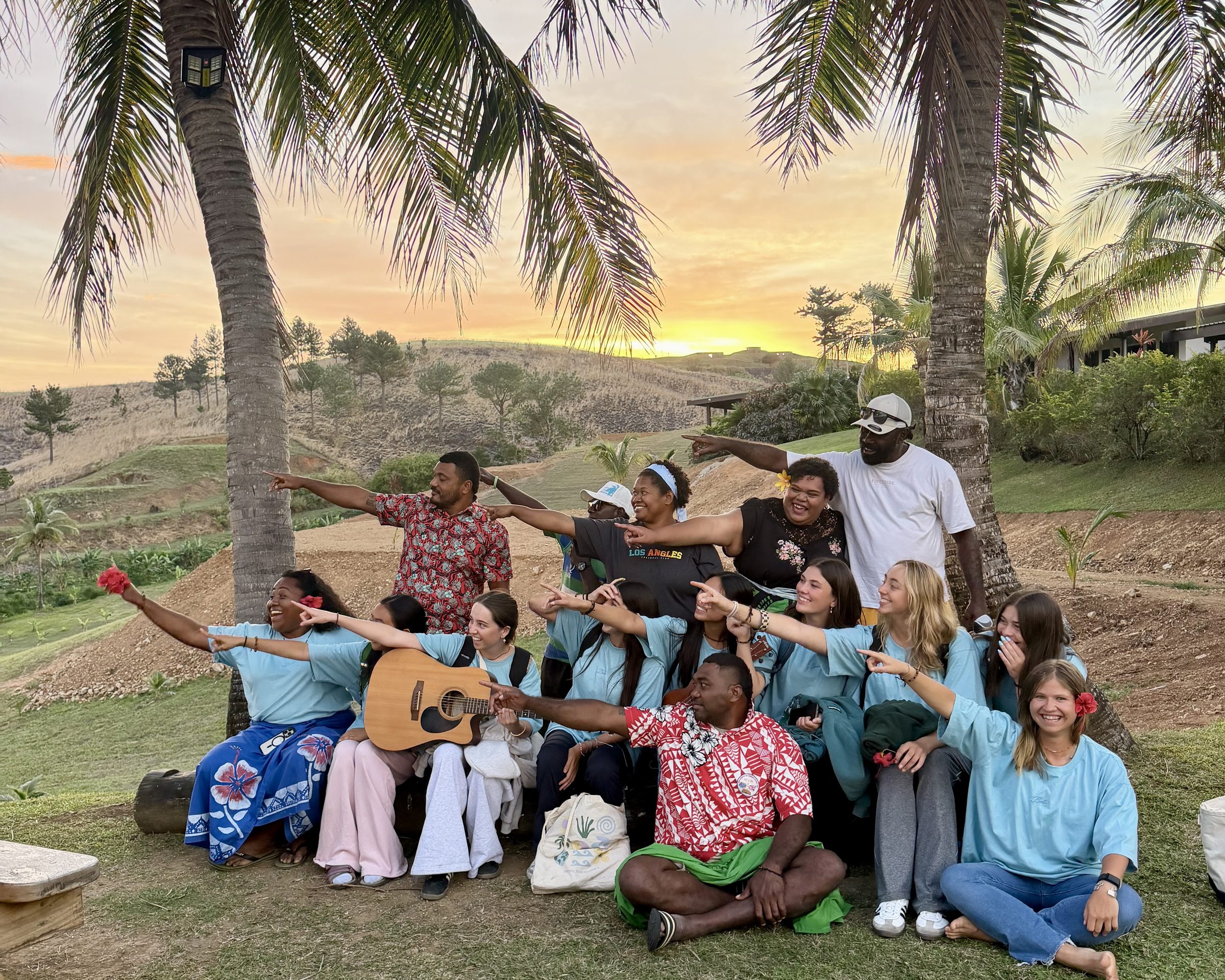 A Rustic Pathways group gathers under palm trees at sunset in Fiji, with a guitar.