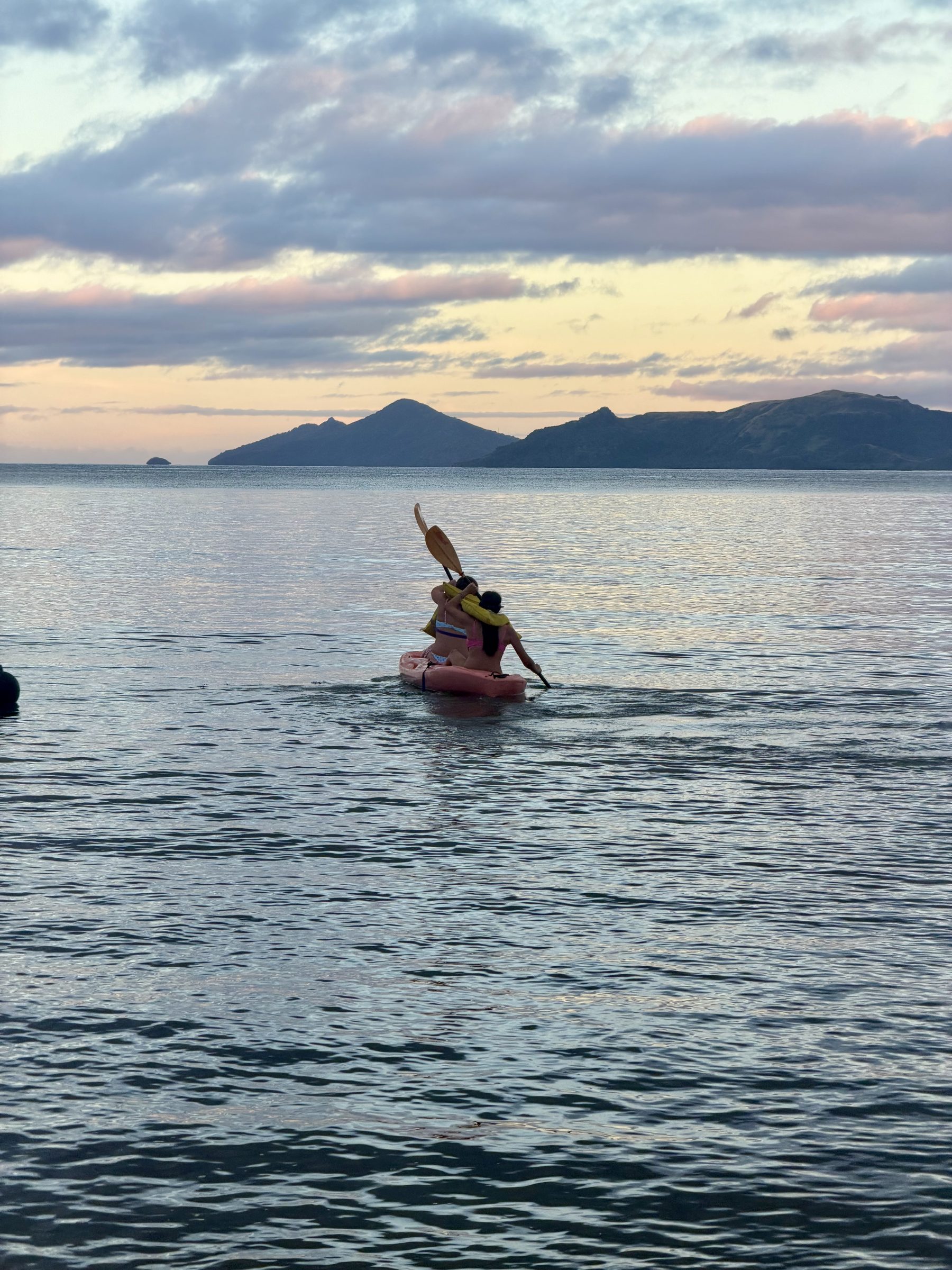 A kayaker paddles toward an island at sunset in Fiji.