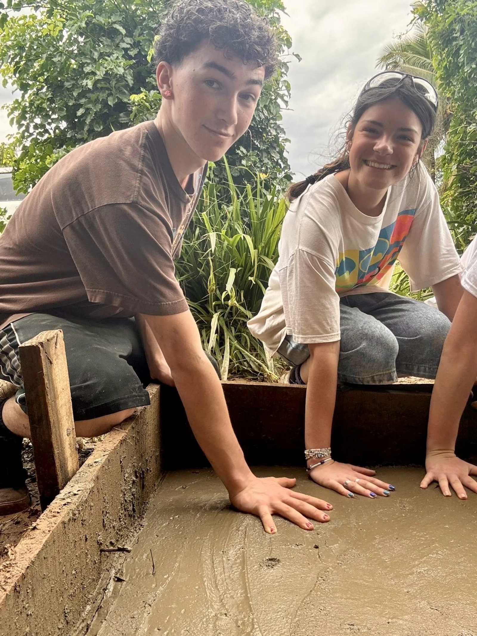 Two students kneel beside a freshly poured concrete form on a service project in Fiji