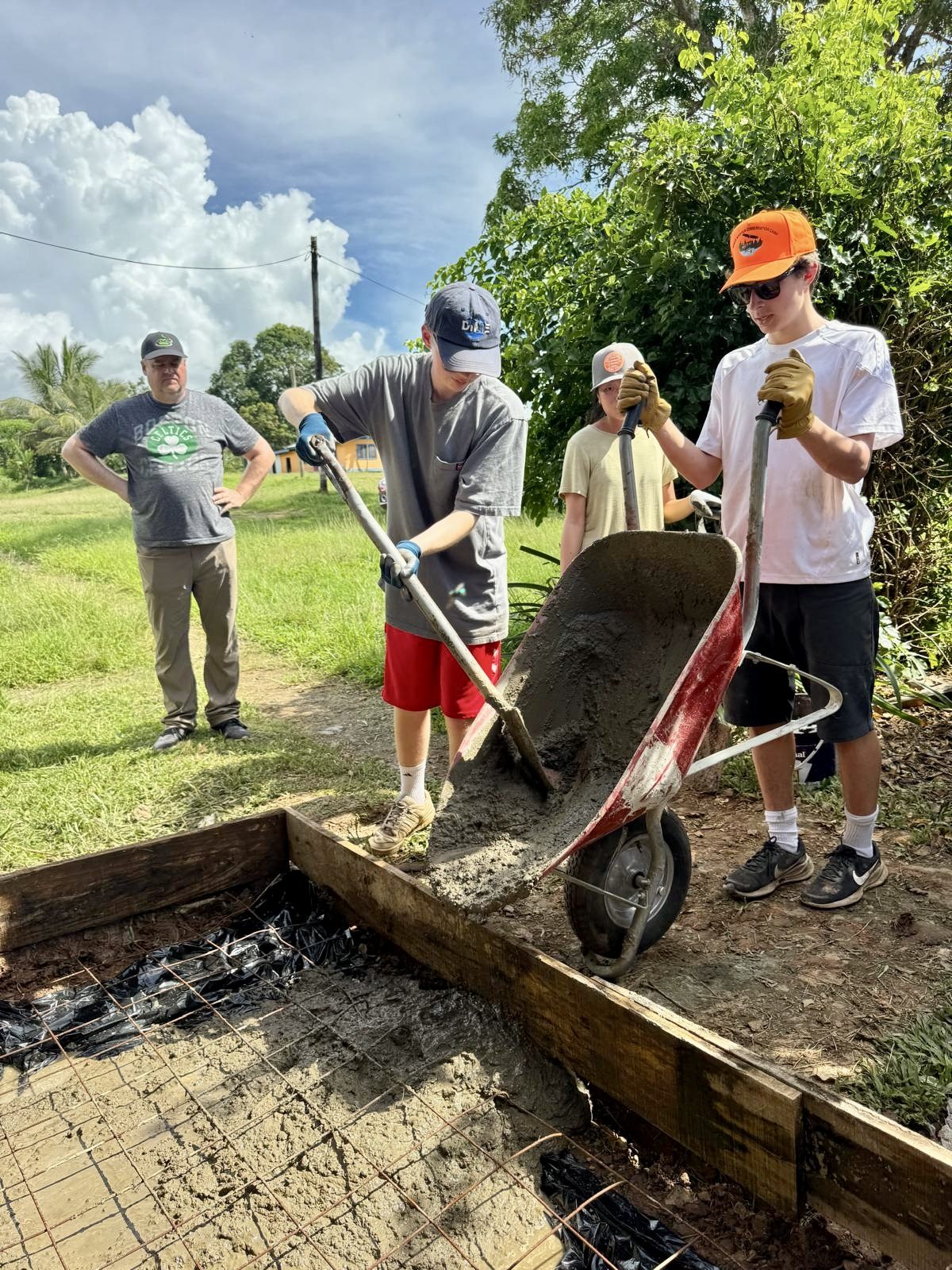 Students move cement by wheelbarrow and shovel on a village build in Fiji.