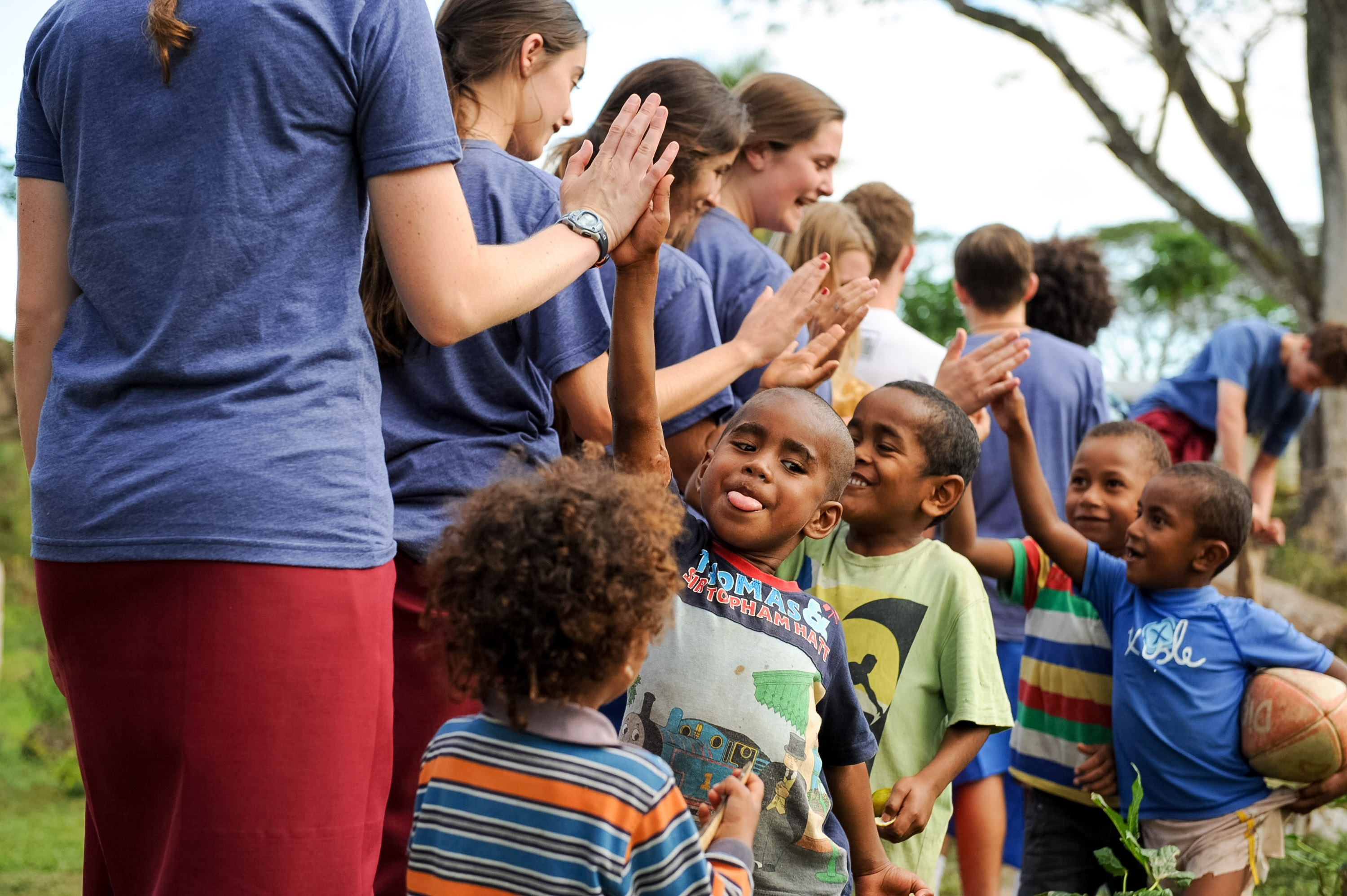 Students high-five local children in a line outdoors