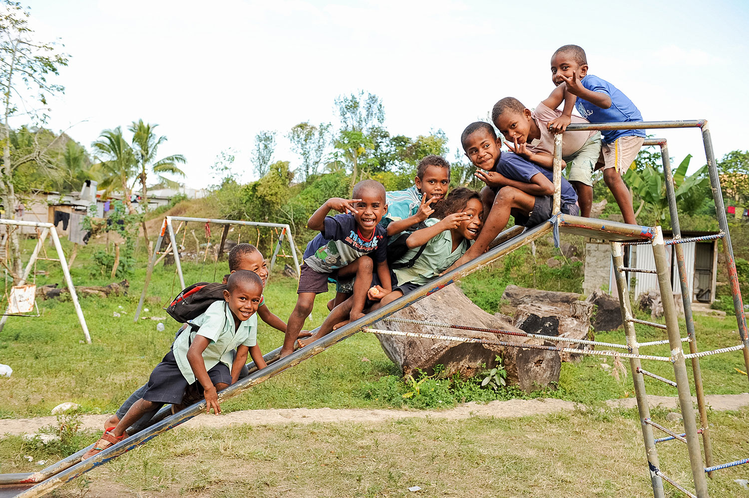 Local children play on a metal slide in a grassy yard