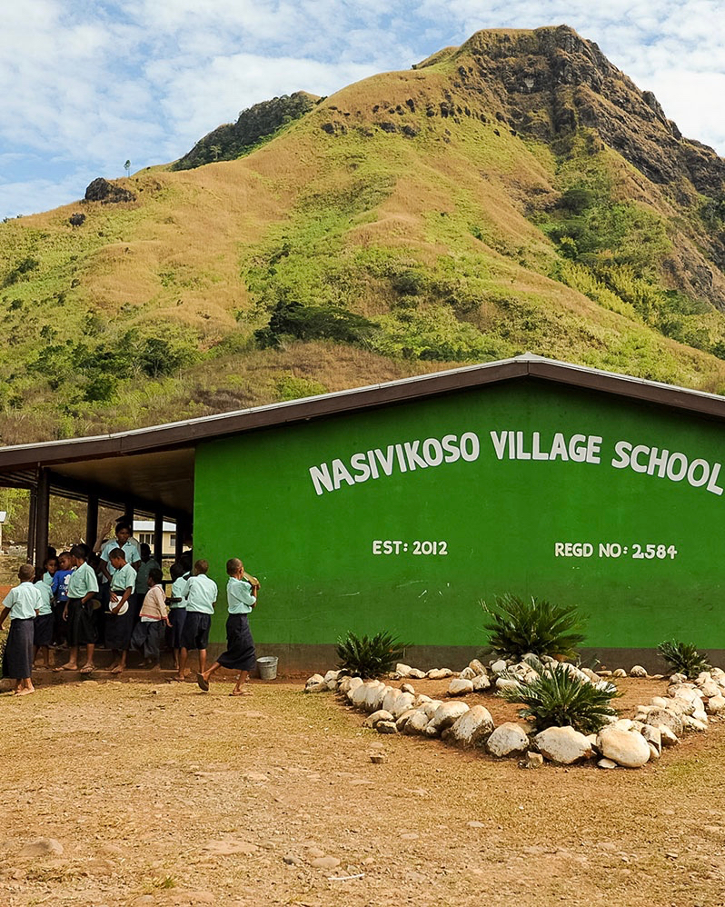 A school trip stop at Nasivikoso Village School finds children gathered outside beneath a green mountain