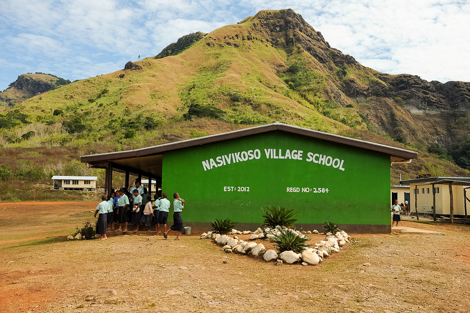 Students gather outside the green Nasivikoso Village School building beneath a mountain backdrop