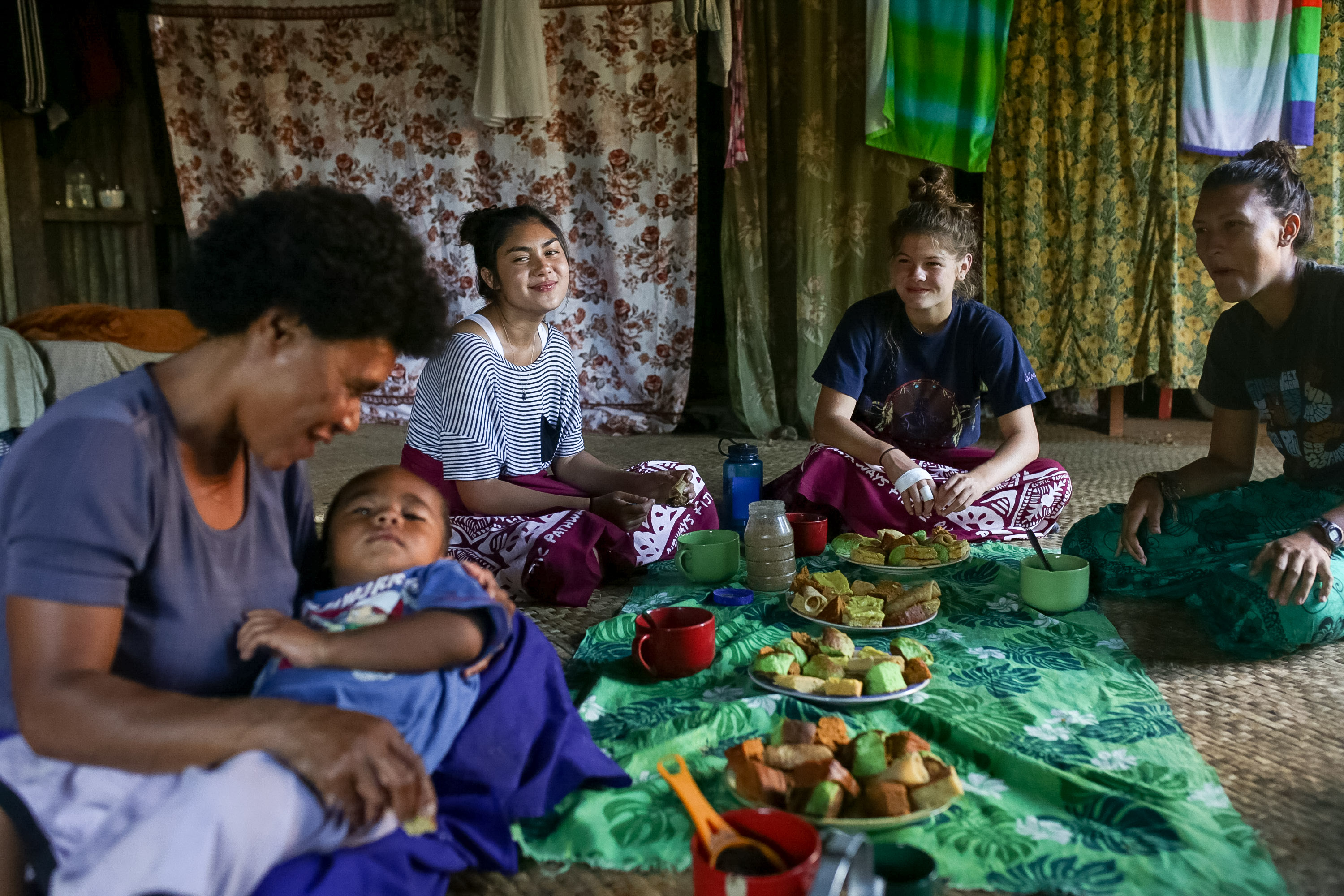 Students share a meal with a Fijian host family seated on the floor of a village home