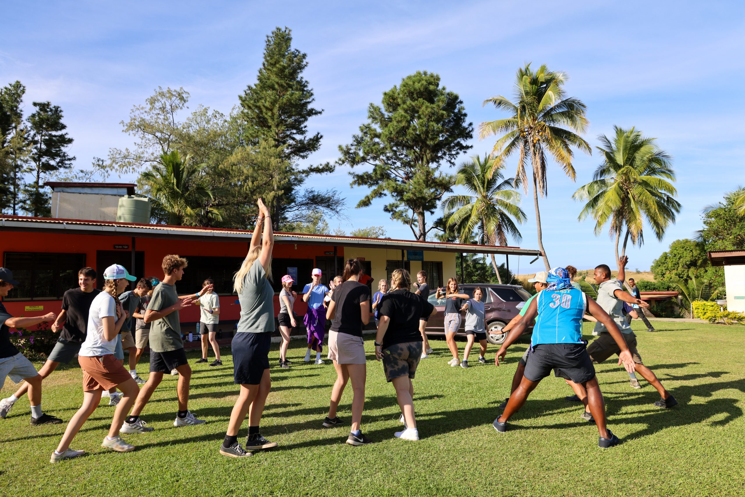 Students stretch and warm up on a grassy lawn lined with palm trees