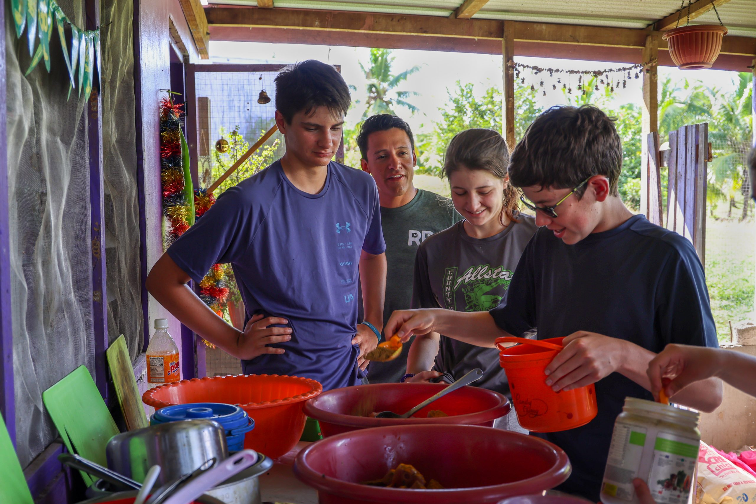 Students prepare food together in bowls at an open-air kitchen with a local host