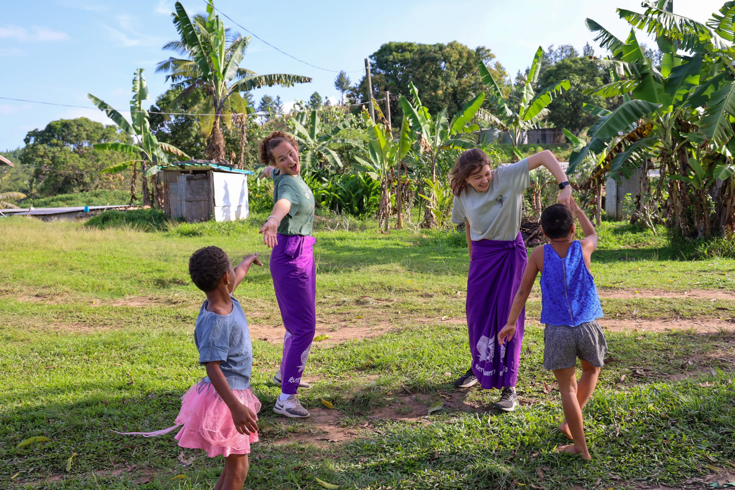 Students dance and play with local children on a grassy field in Fiji