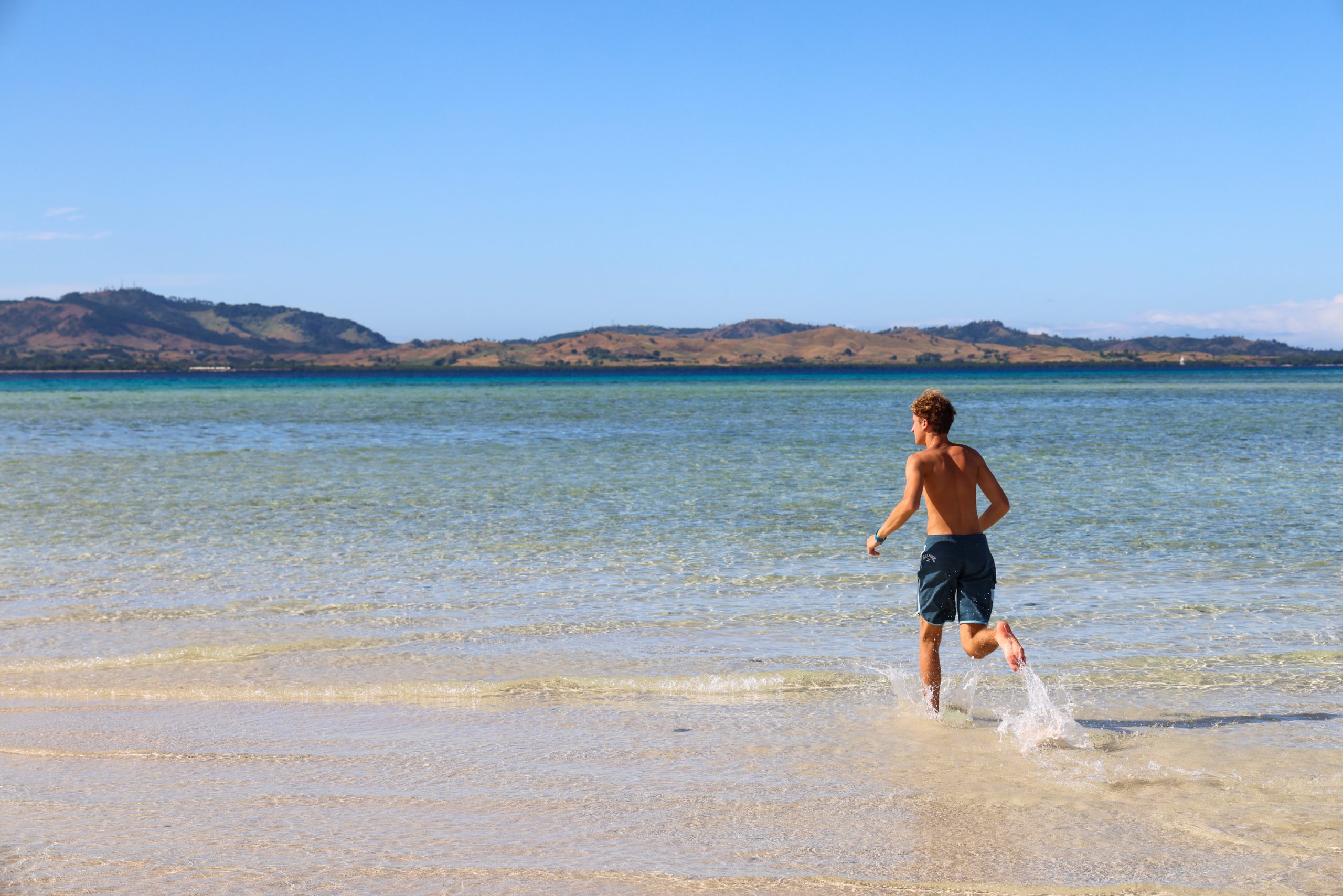 Teen travelers run through shallow water along a tropical shoreline