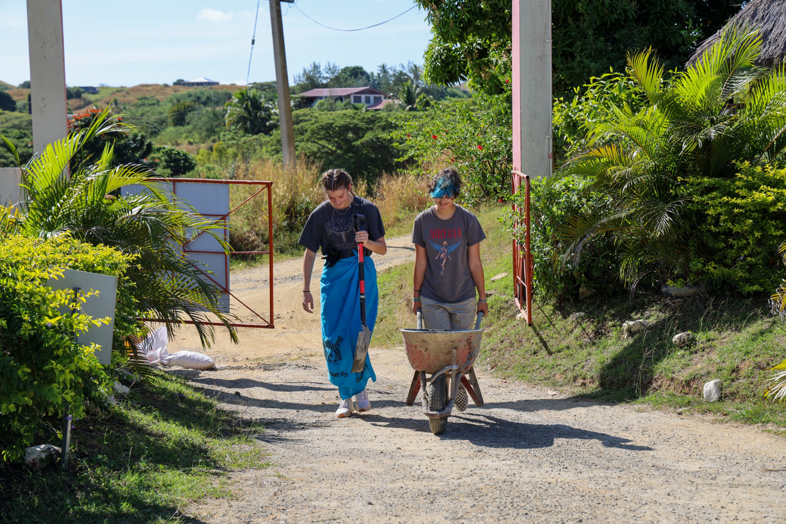 Students push a wheelbarrow along a dirt road on a community service project in Fiji