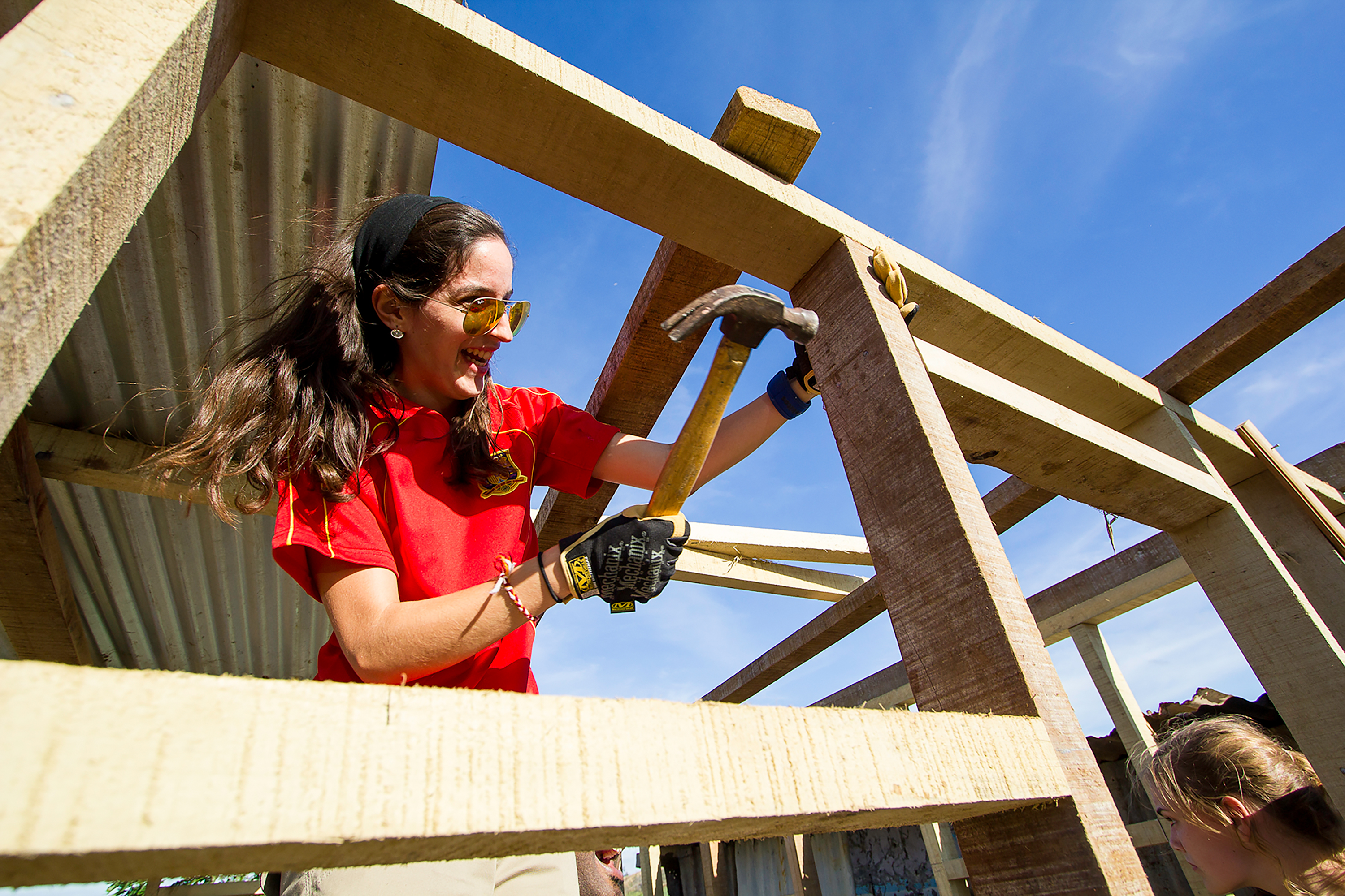 A student hammers a nail into wooden roof framing at a construction site