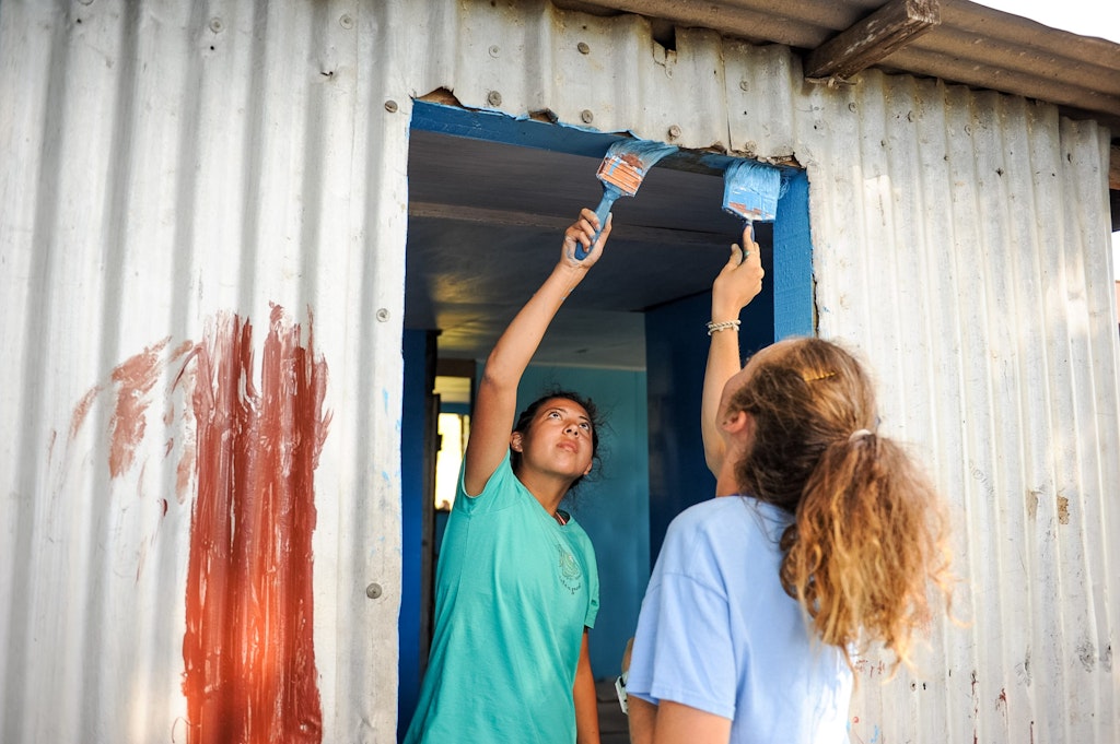 Teens painting a classroom together as part of a childcare volunteering abroad program improving local education spaces.