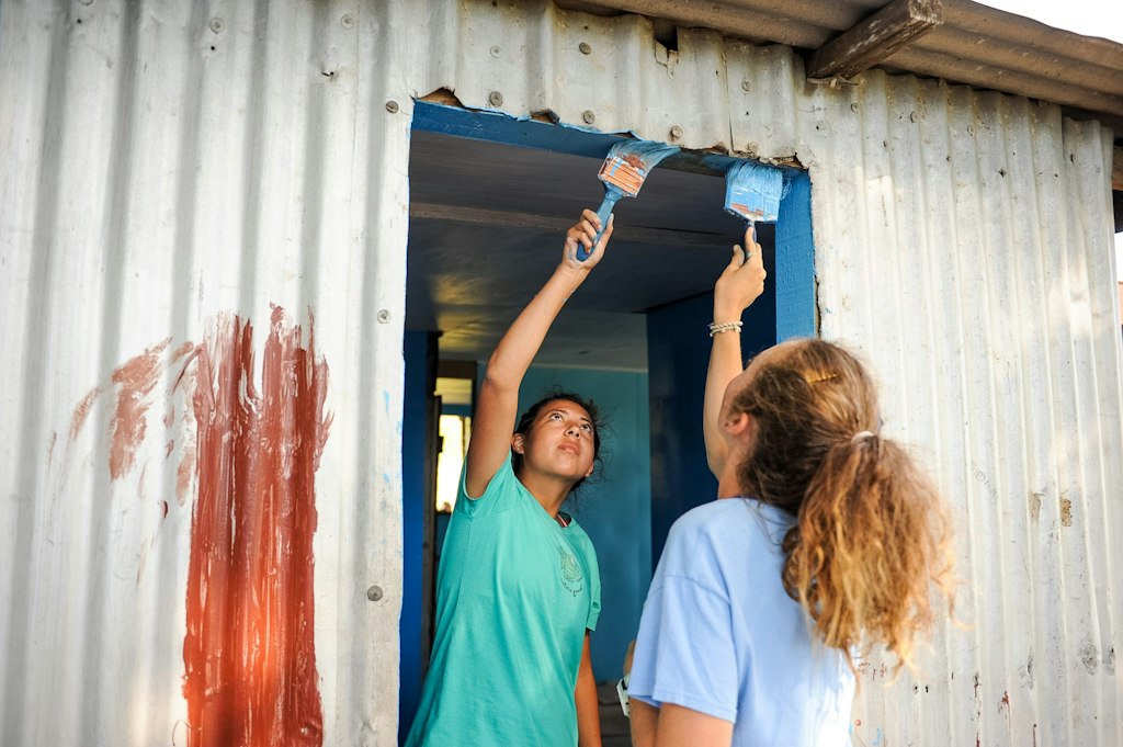 Students participating in an ethical voluntourism project, painting a community building as part of a sustainable service initiative.