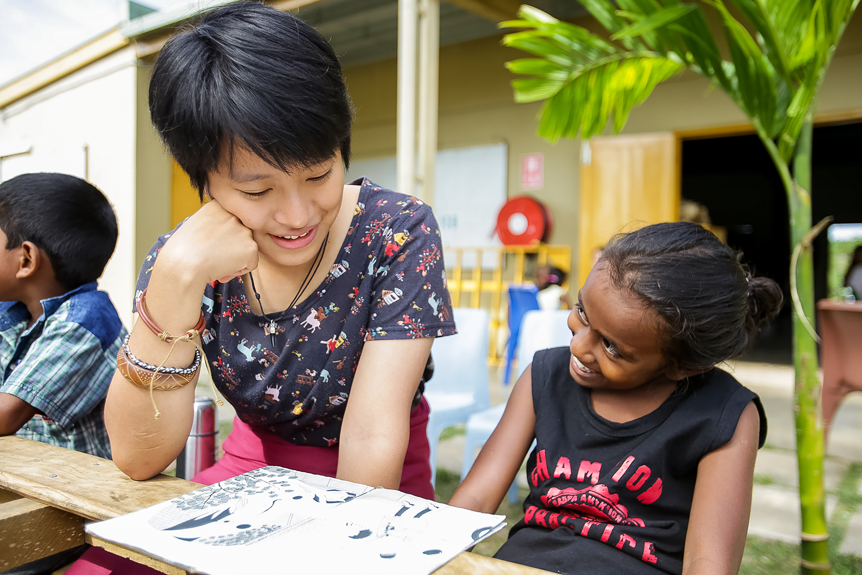 A student reads a picture book with a local child at an outdoor table
