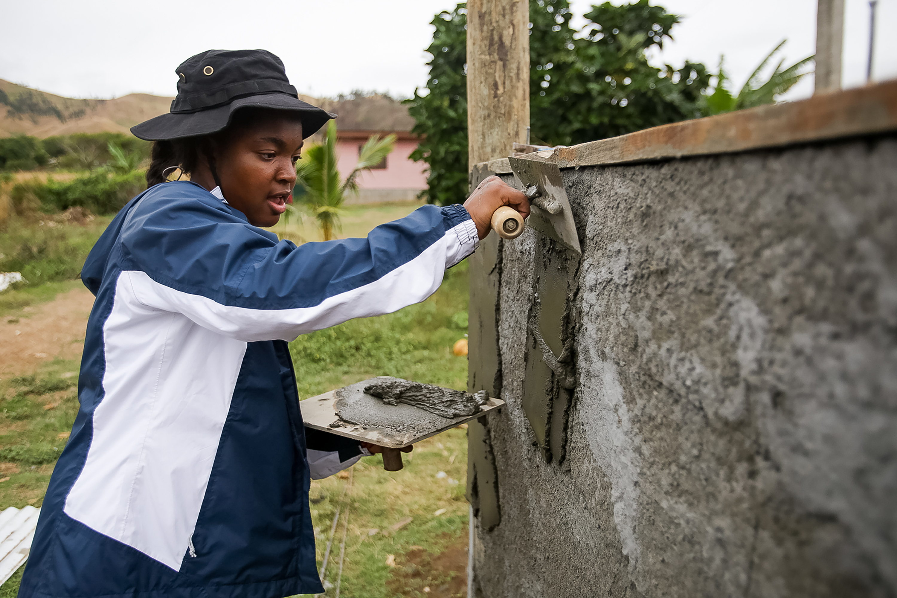 Students smooth wet concrete on a wall with a trowel during a community service project