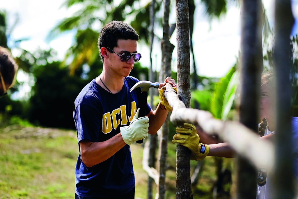 Student participating in childcare volunteering abroad, building wooden structures alongside teammates in a tropical setting.