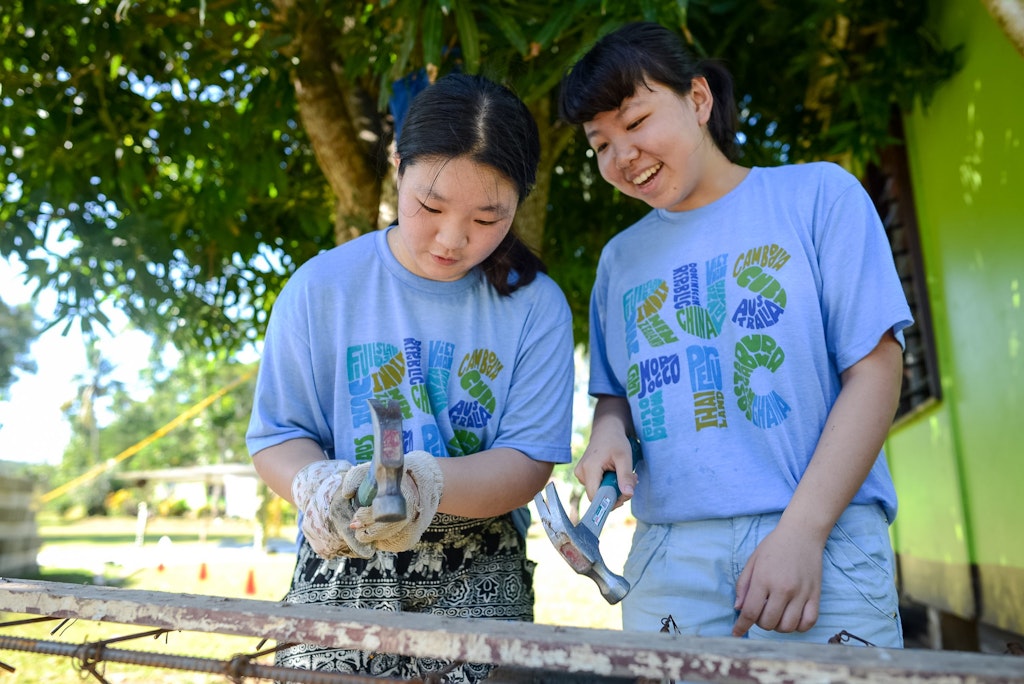 Two students smiling while using hammers during a childcare volunteering abroad project focused on community construction.