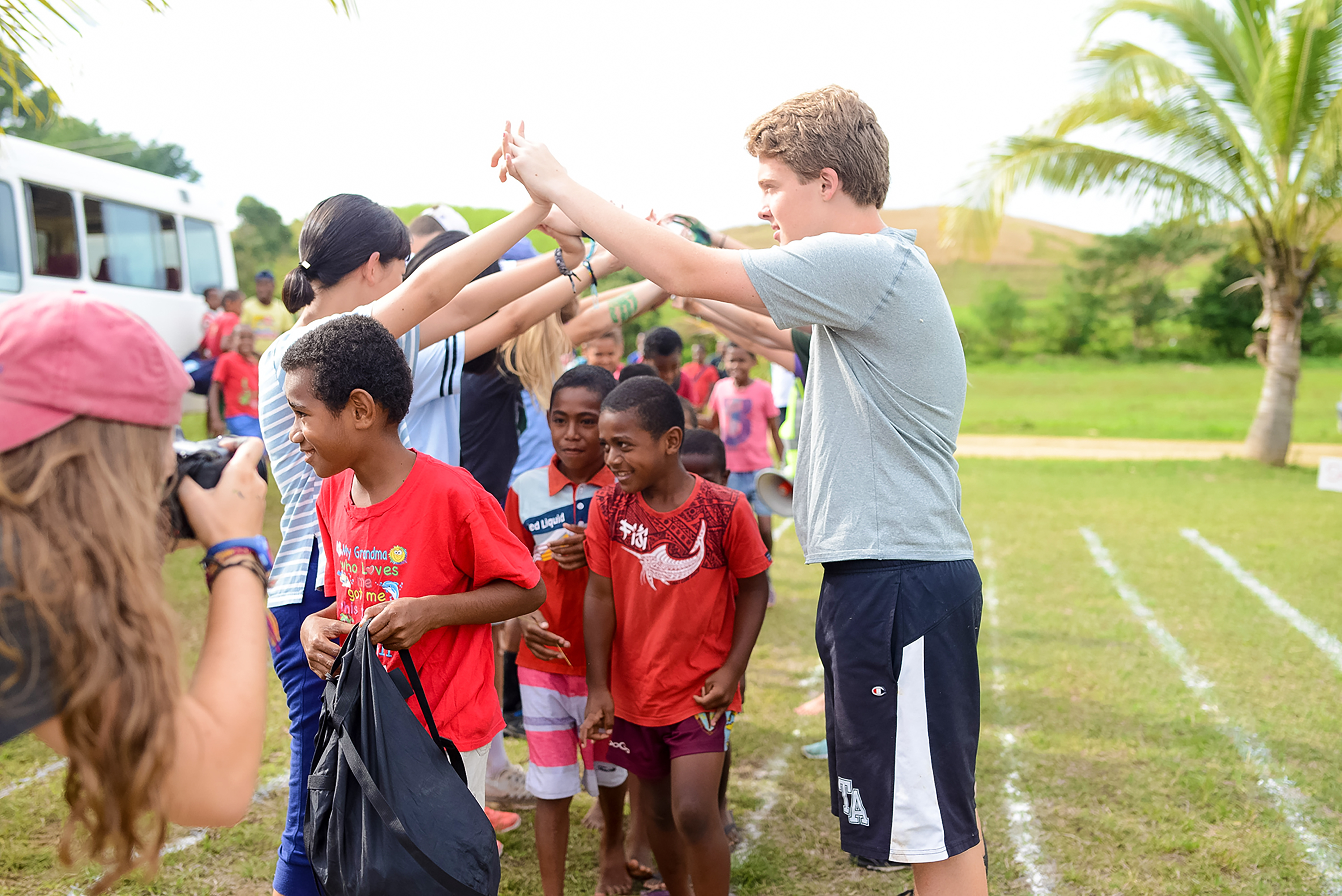 Students high-five local children on a grassy field during a village visit