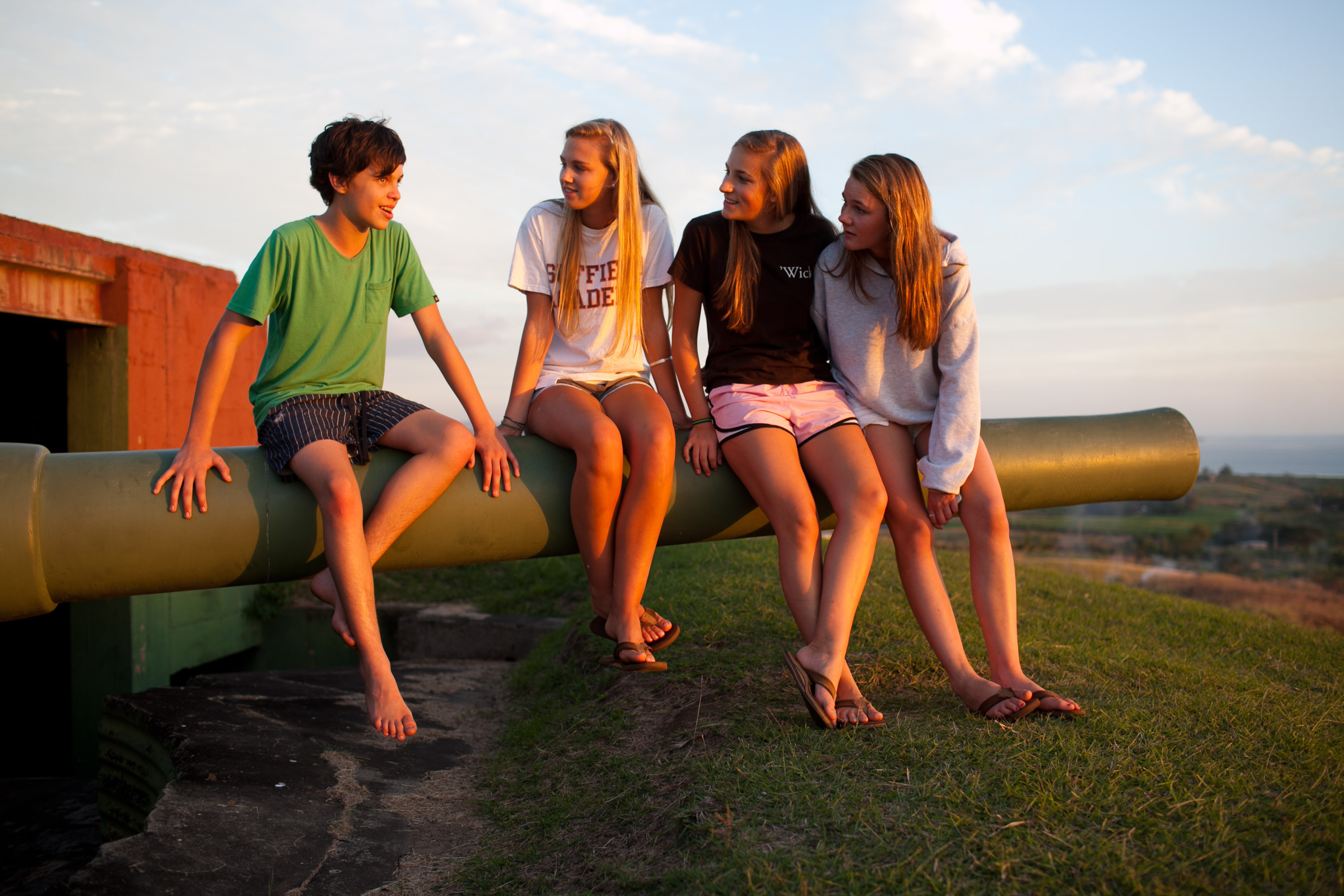 Students sit together on an old cannon overlooking the coastline at sunset