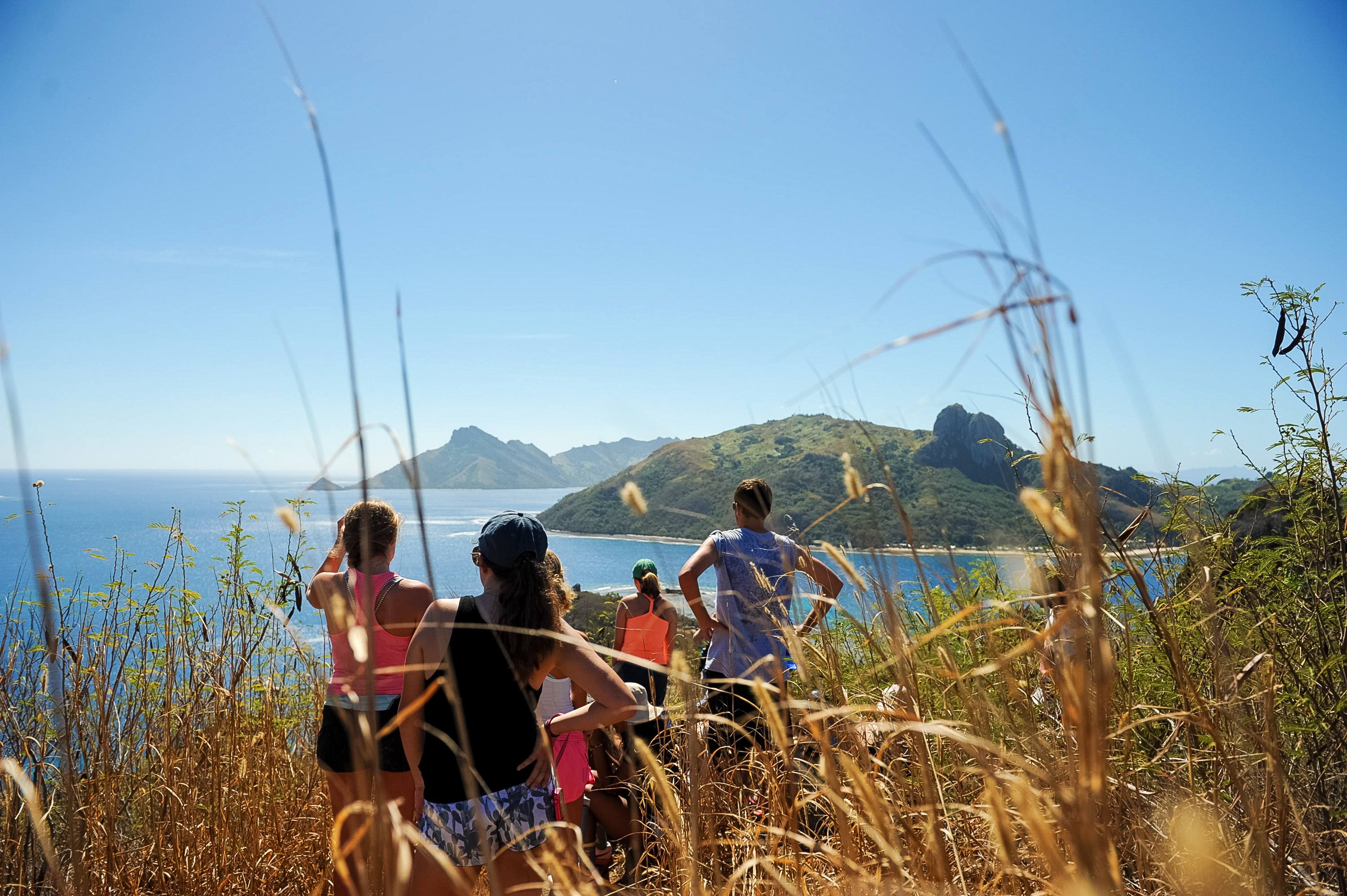 Students pause on a grassy hillside overlooking Fiji's coastline and mountains