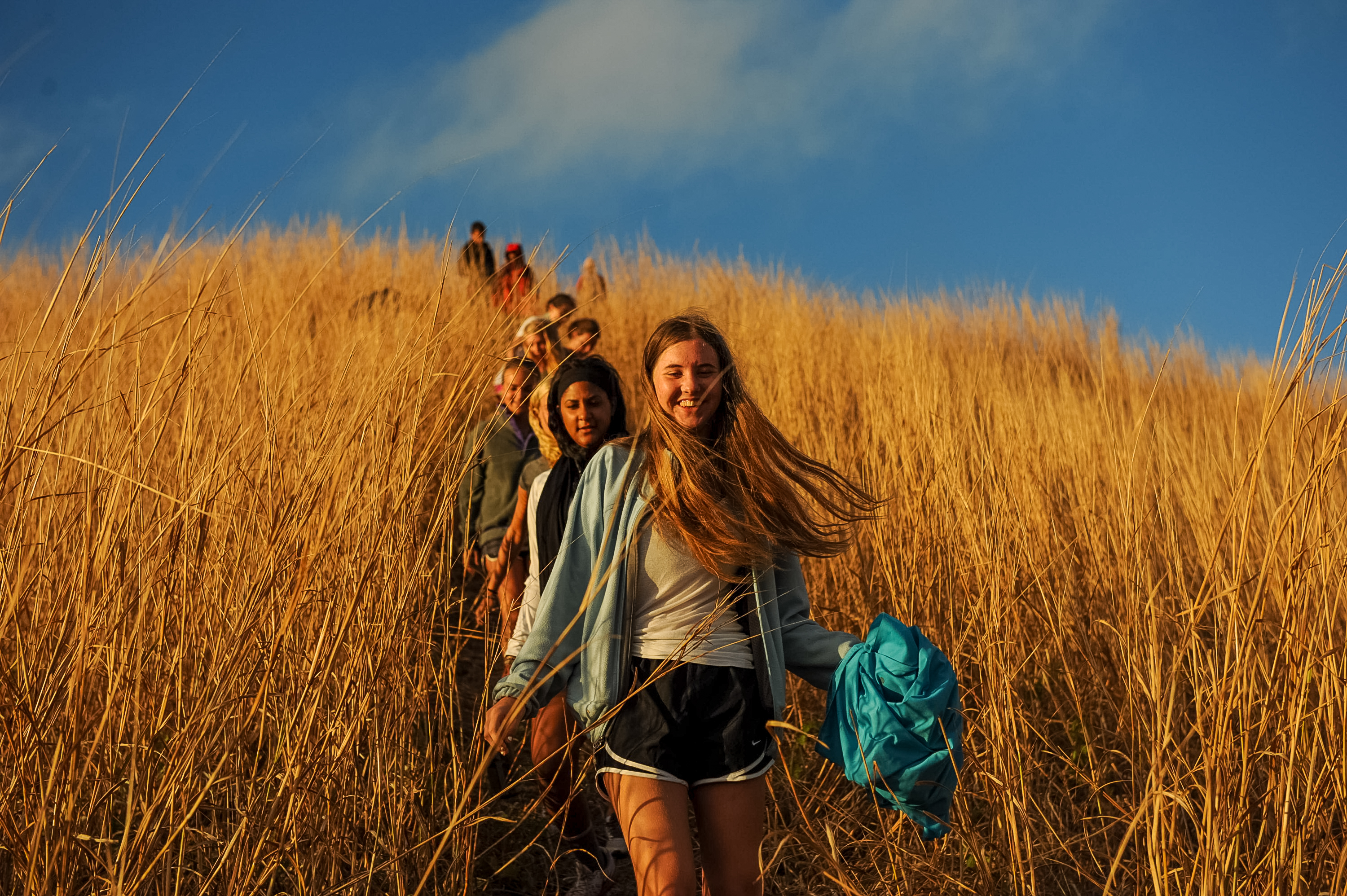 Students hike single file through tall golden grass on a hillside
