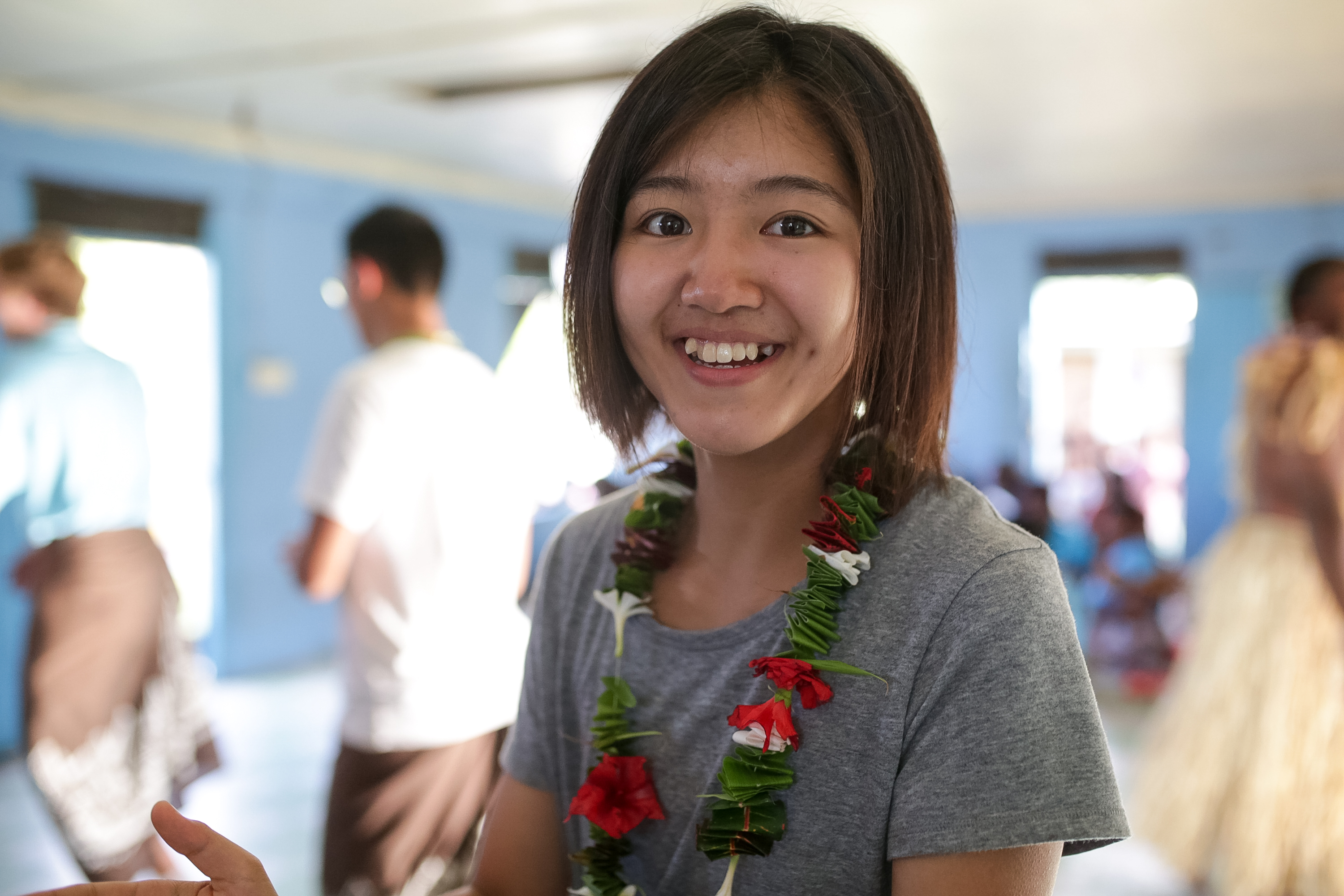 A student wears a floral garland and smiles indoors
