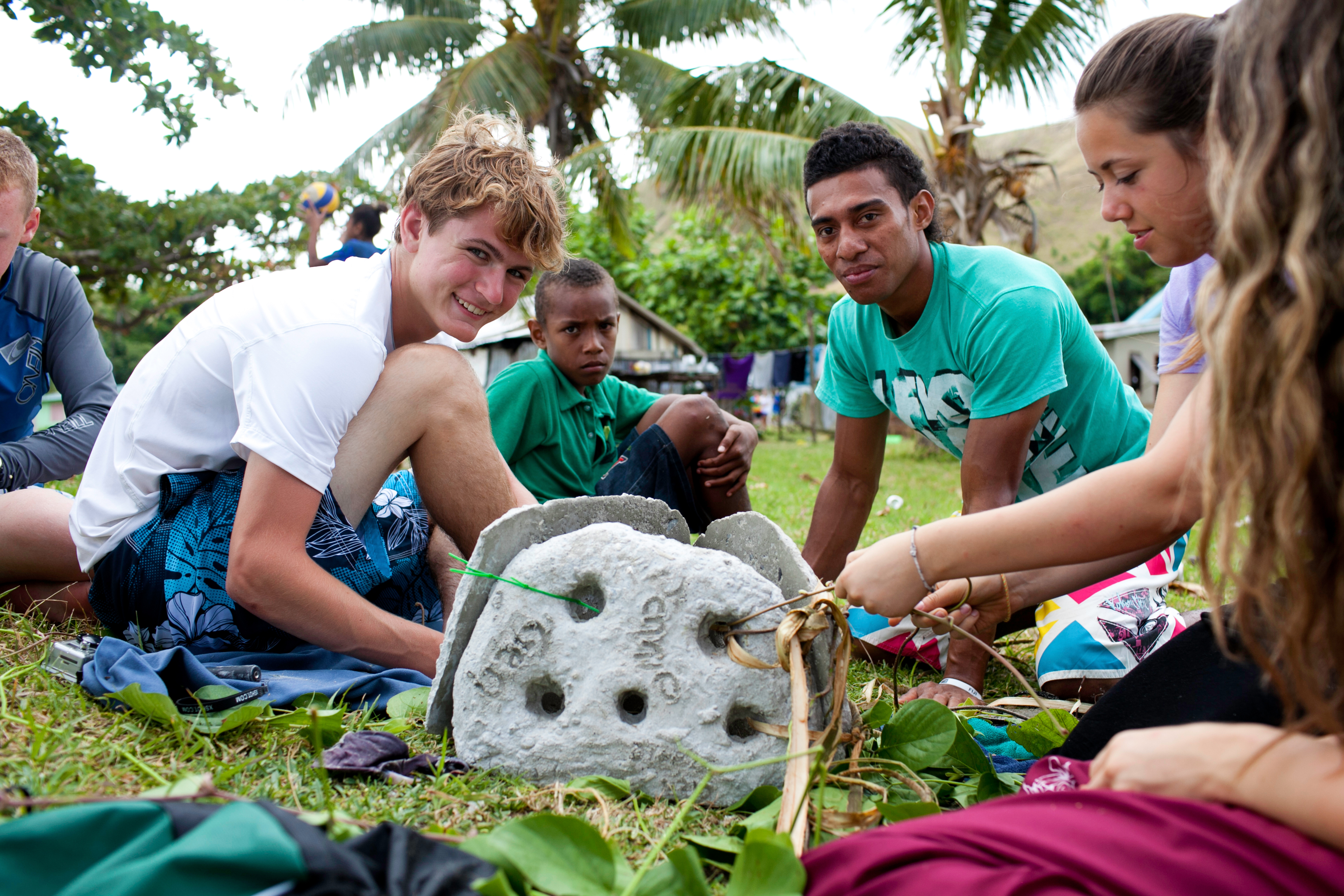Students and local villagers in Fiji gather around a carved stone artifact on the grass