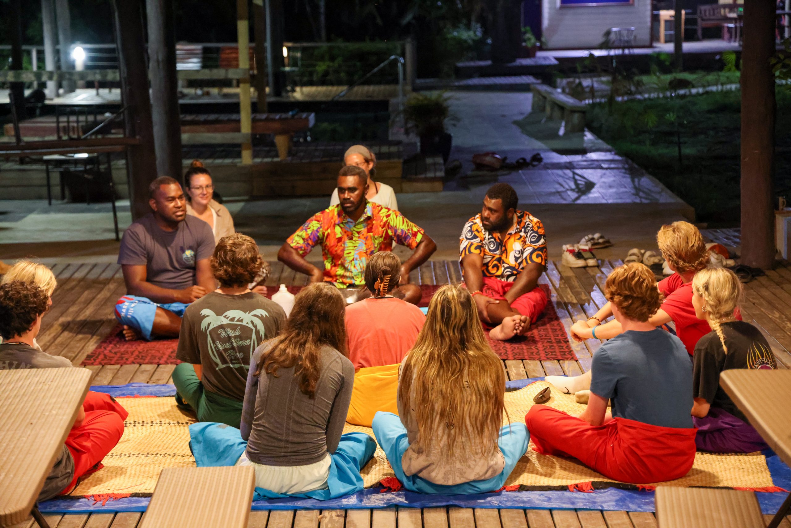 Students sit in a circle on woven mats during an evening talk with Fijian hosts