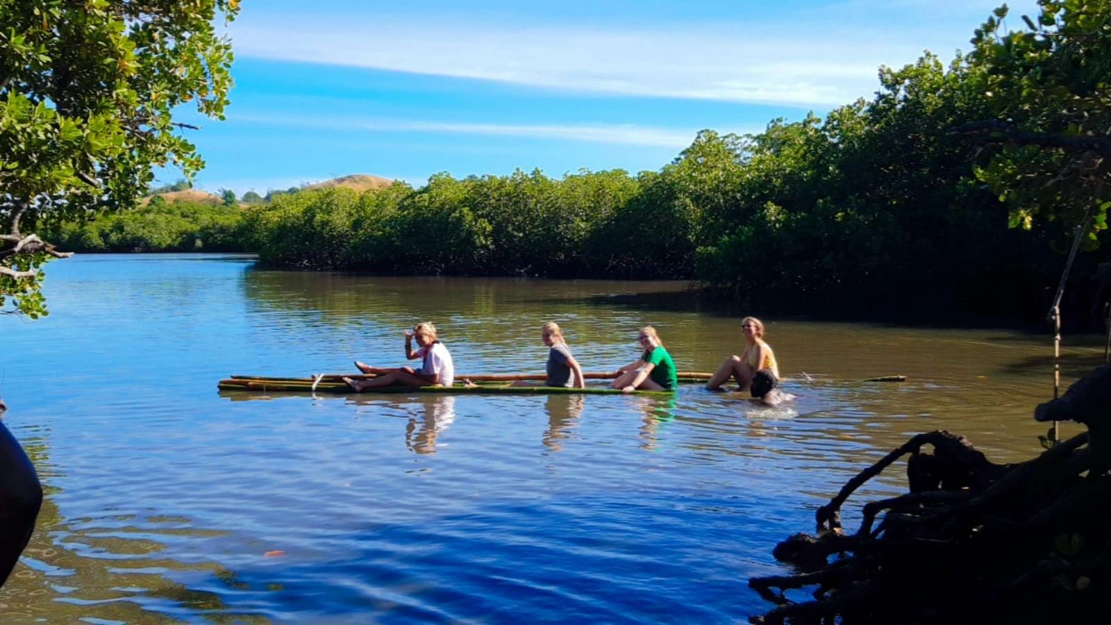 Students paddle a wooden canoe along a calm, mangrove-lined river