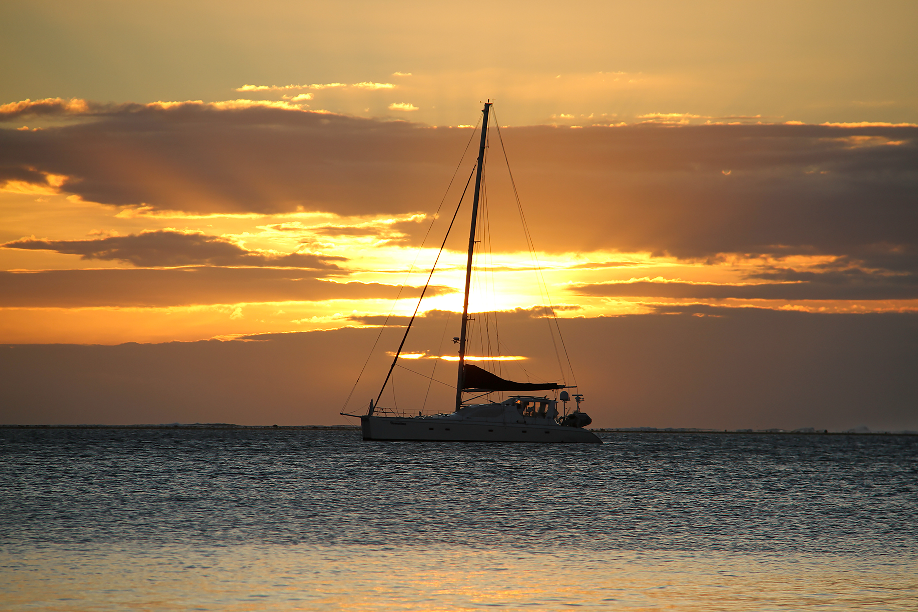 A sailboat drifts on calm water beneath a glowing sunset sky