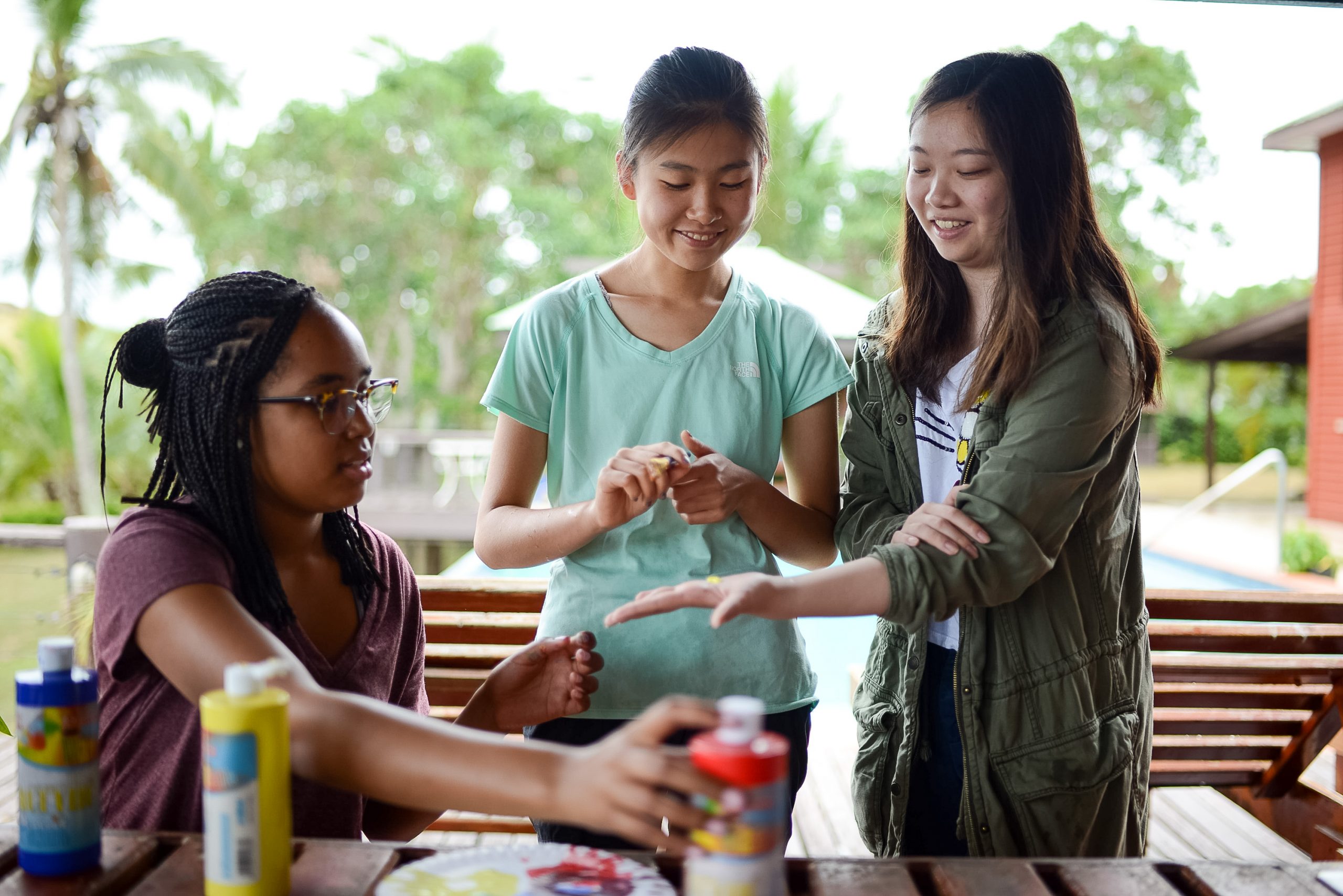 Students gather at an outdoor table with paint supplies near a pool
