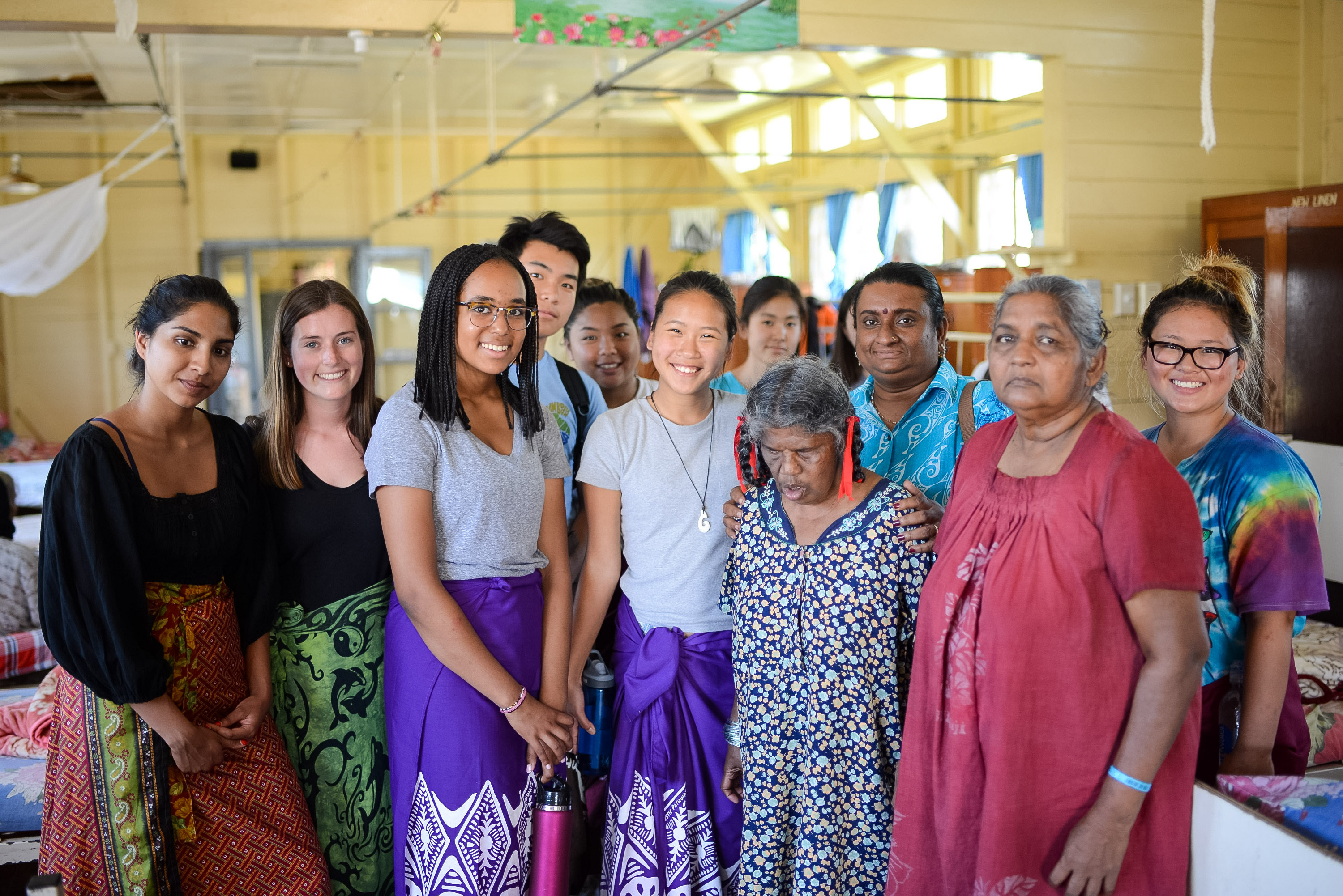 Students pose with local Fijian community members inside a village hall