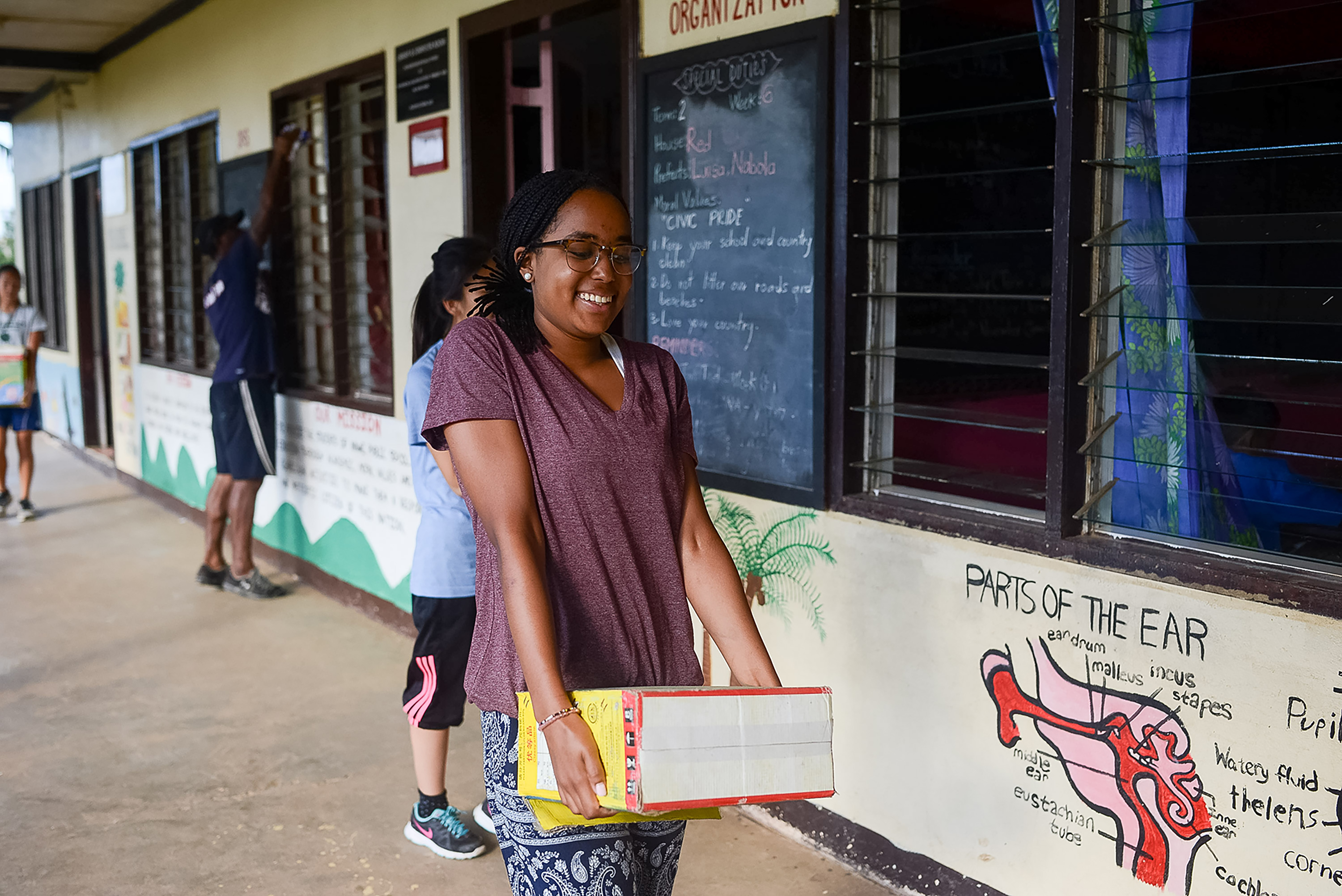 Student travelers carry books along a school walkway painted with educational murals