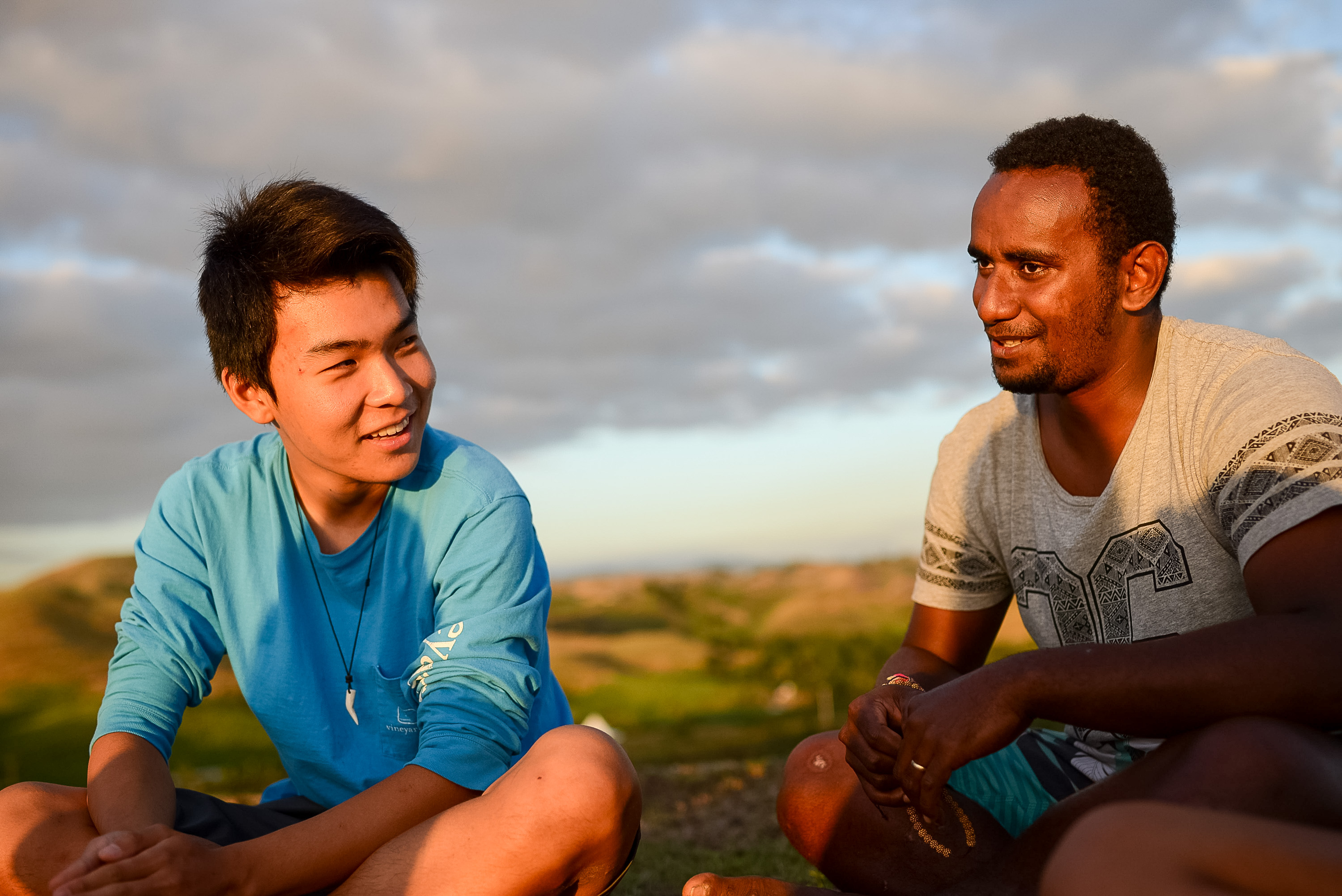 Students sit together on a hillside, chatting as clouds glow at sunset