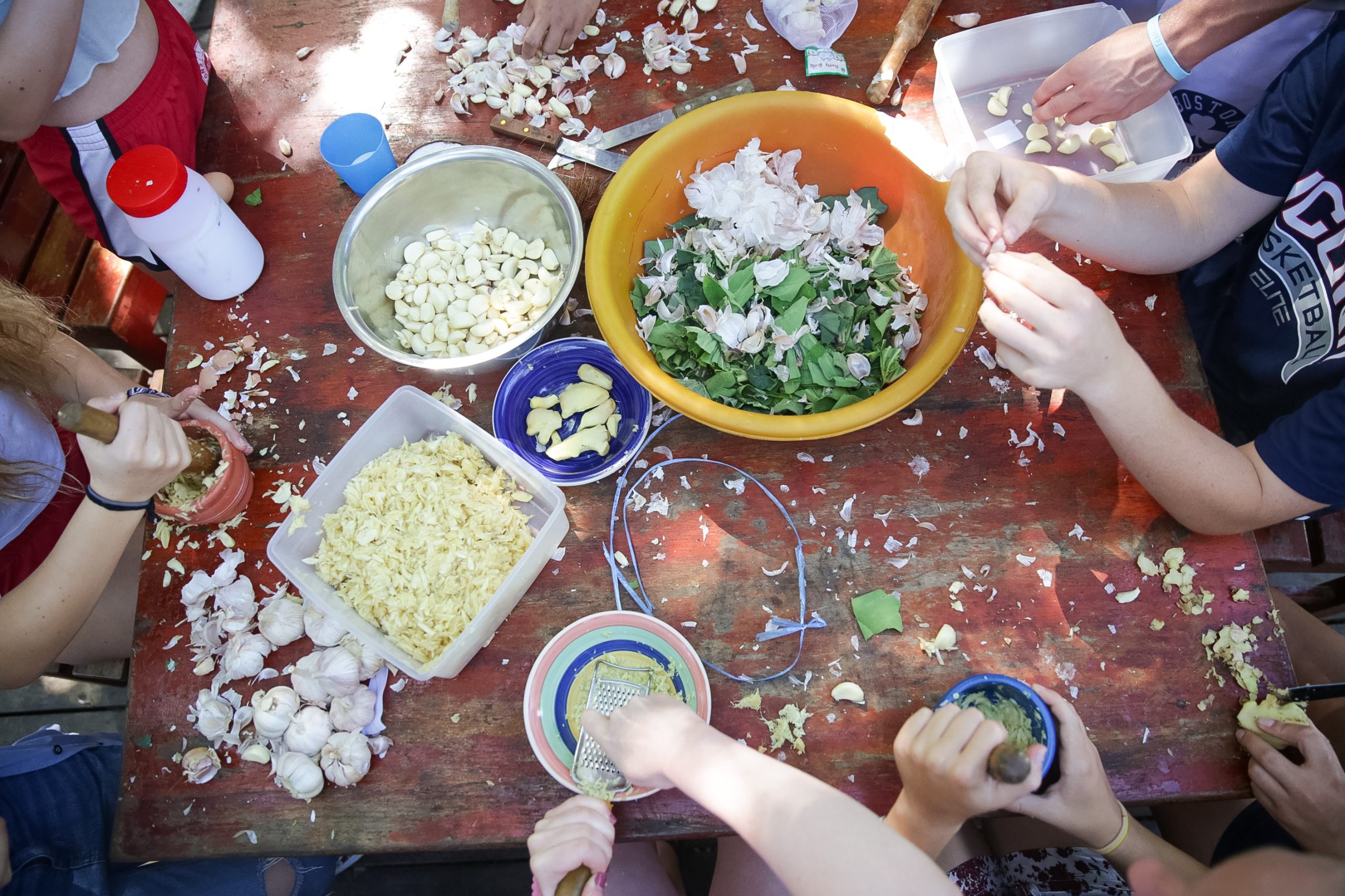 Students prepare fresh ingredients in bowls at a wooden outdoor table