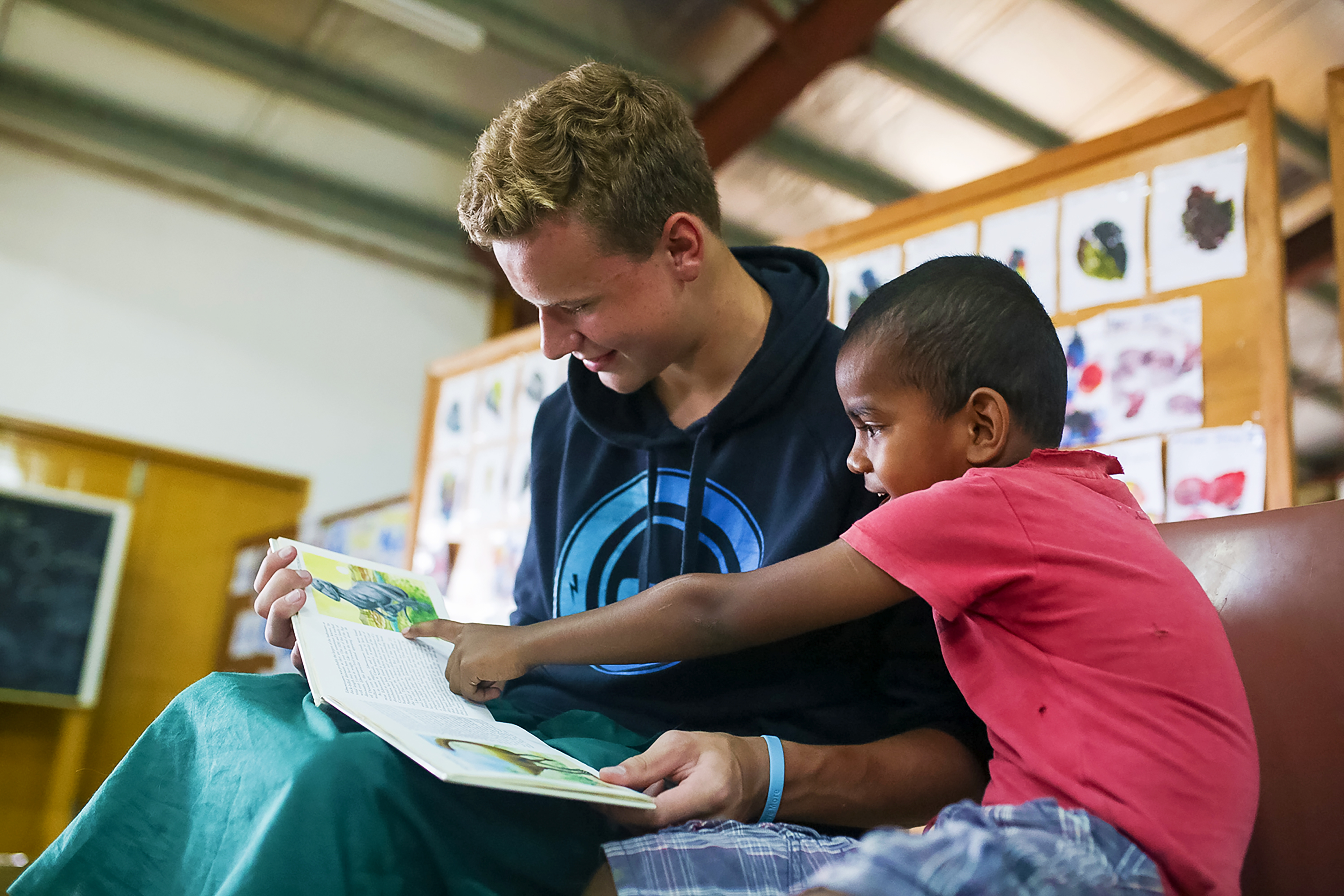 Student volunteer helping a young boy read a book.