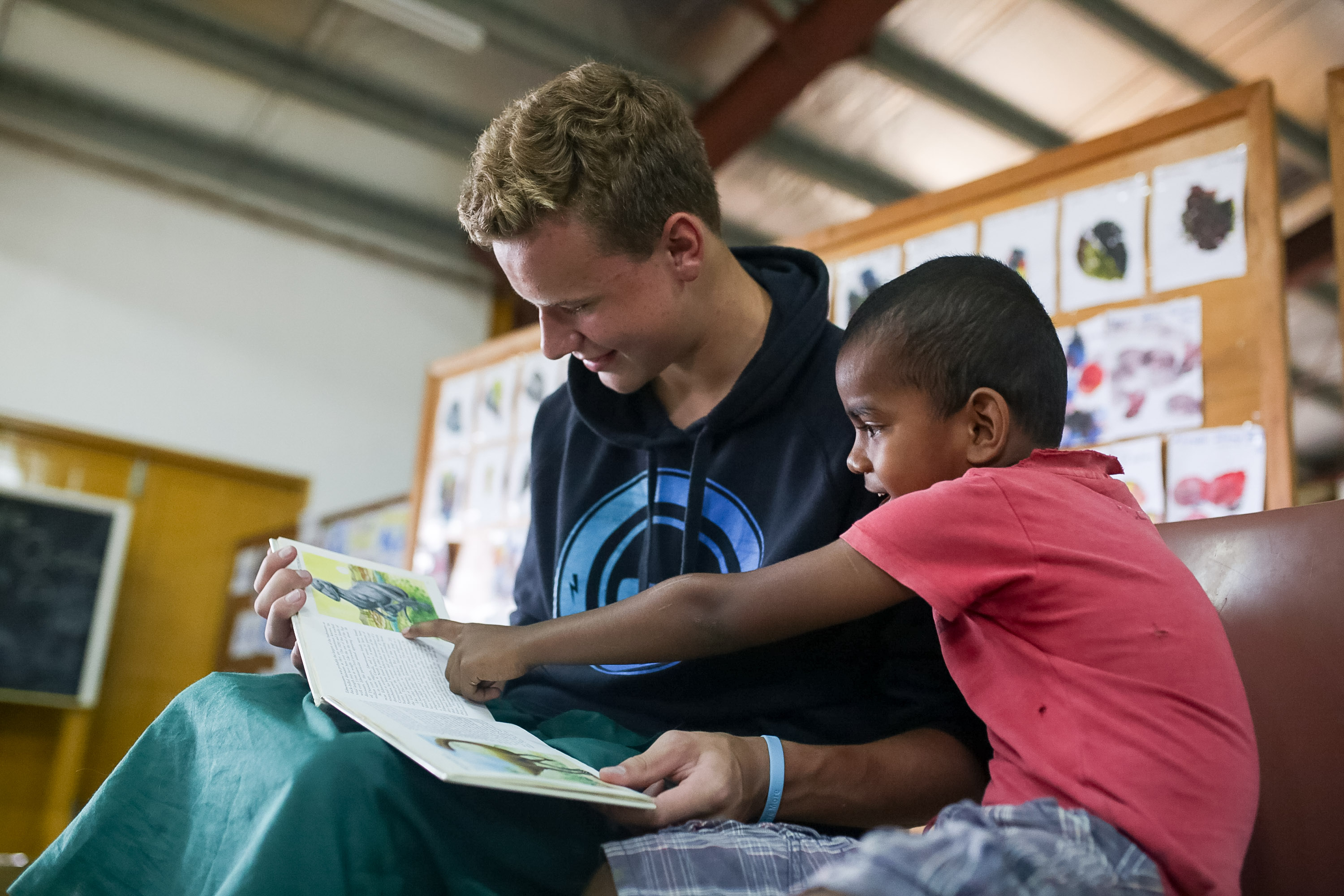 A student reads a picture book with a young child on a couch