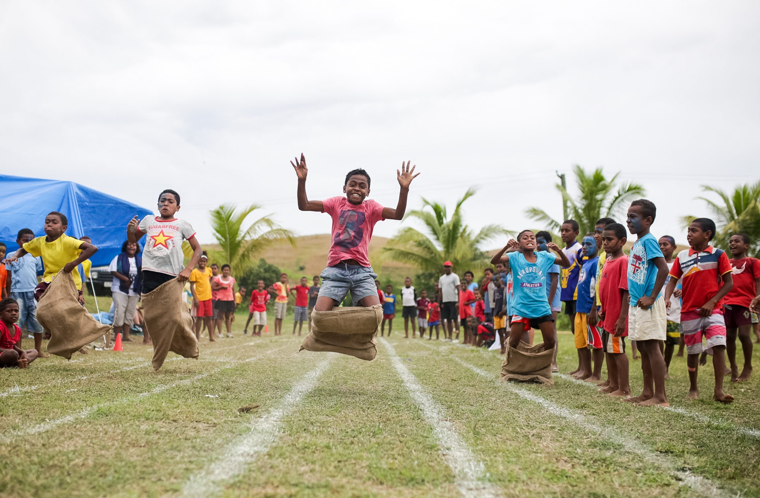 Children race in sack-jumping games on a grassy field in Fiji