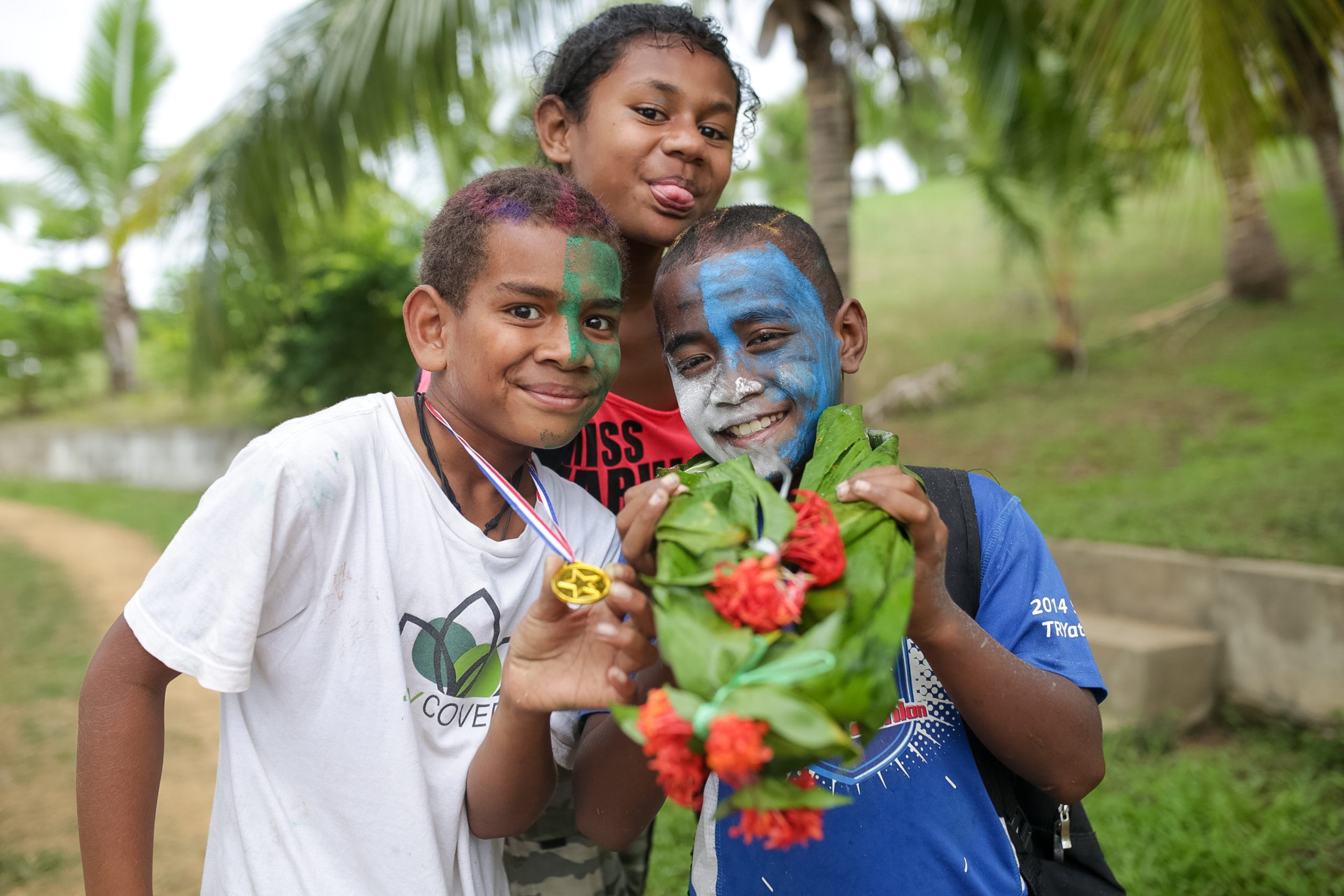 Children with painted faces hold a handmade flower garland outdoors