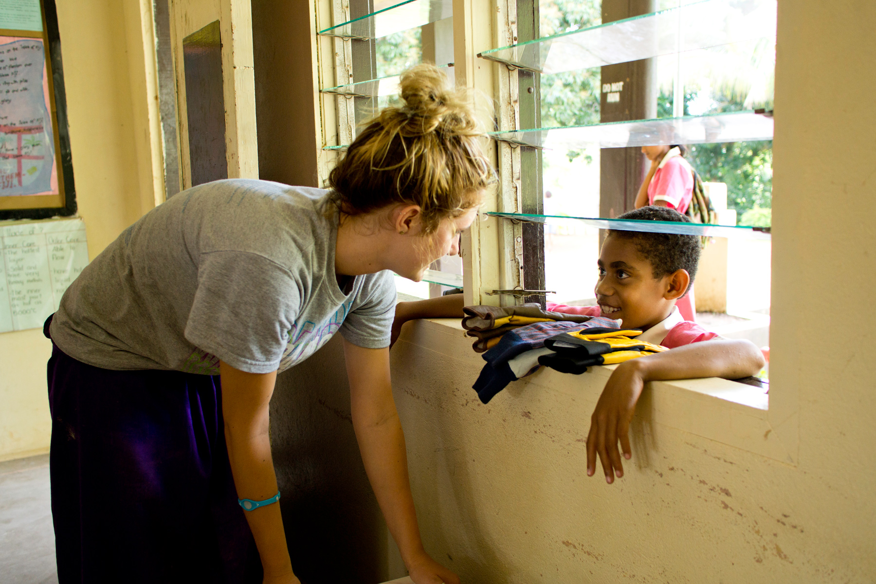 A student leans through a window to talk with a local child