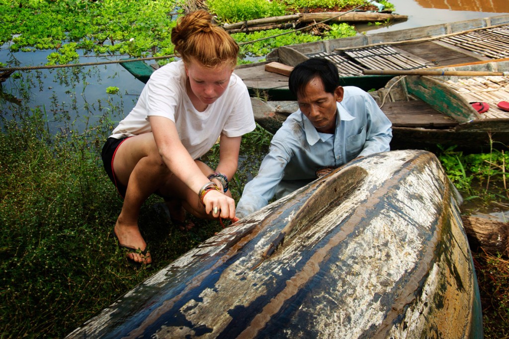 A student and a local man examine a wooden boat hull near a floating village