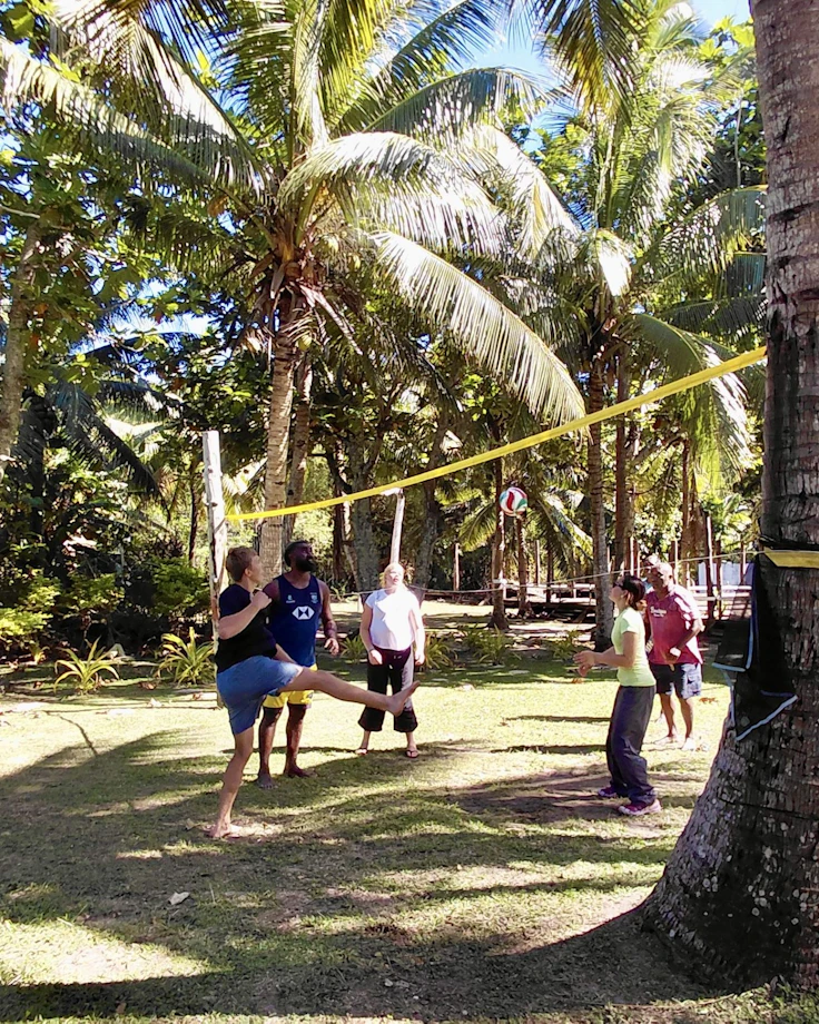 Teen travelers and villagers play volleyball over a net strung between coconut palms in Fiji