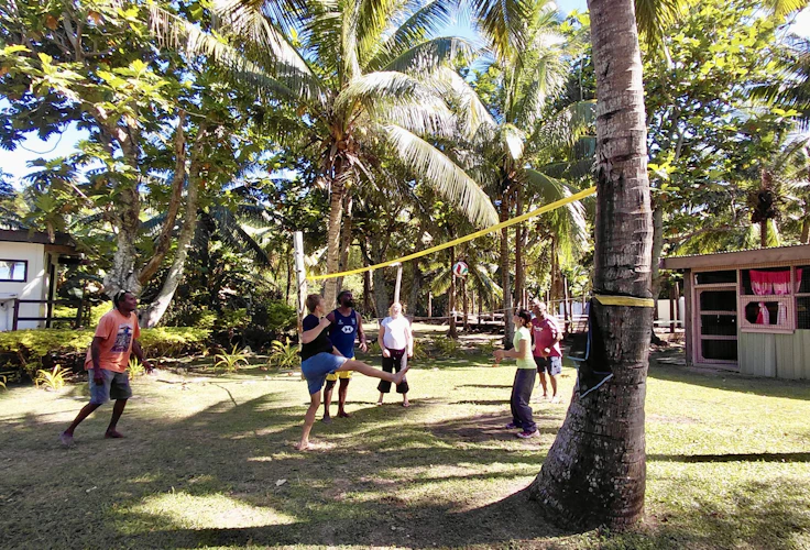 Teen travelers and villagers play volleyball over a net strung between coconut palms in Fiji