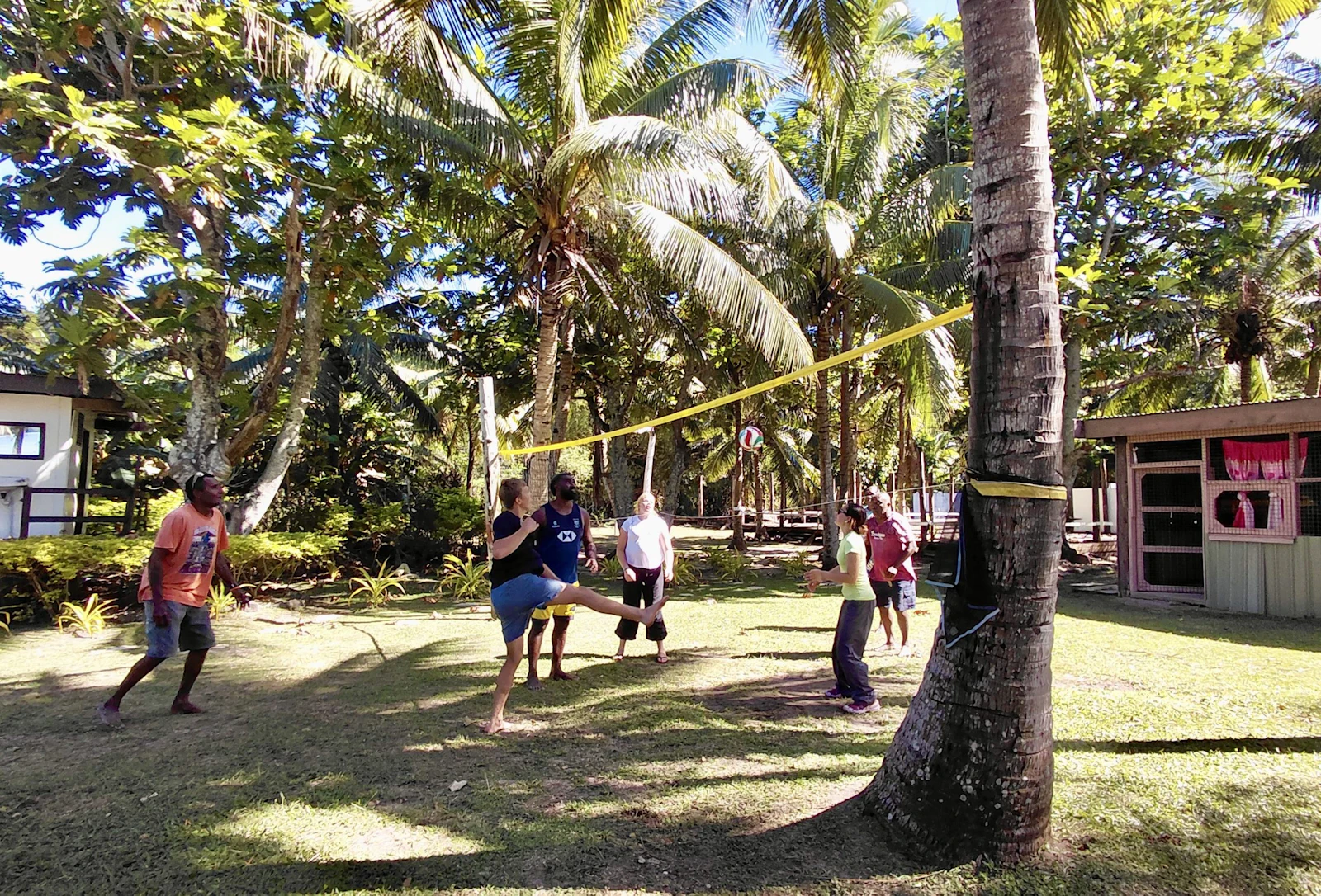 Teen travelers and villagers play volleyball over a net strung between coconut palms in Fiji