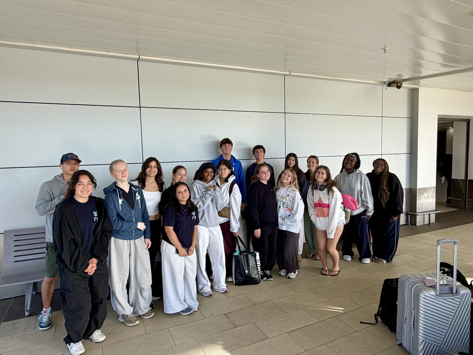 Teen travelers stand together with their luggage in an airport concourse at the start of the program
