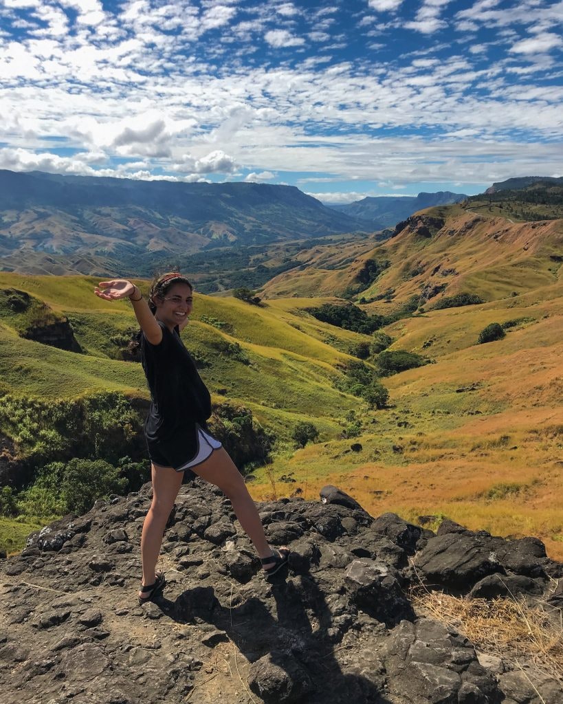 Female student standing on a hilltop with scenic Fijian landscape in the background