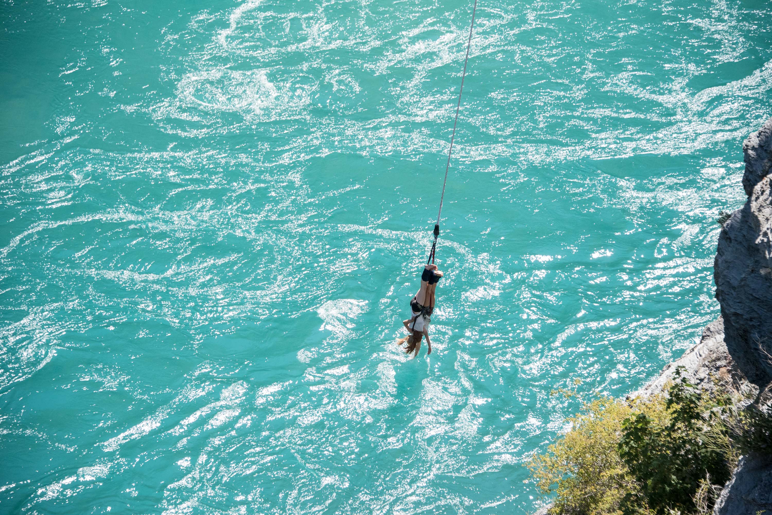 A student swings from a rope over turquoise river water beside a cliff